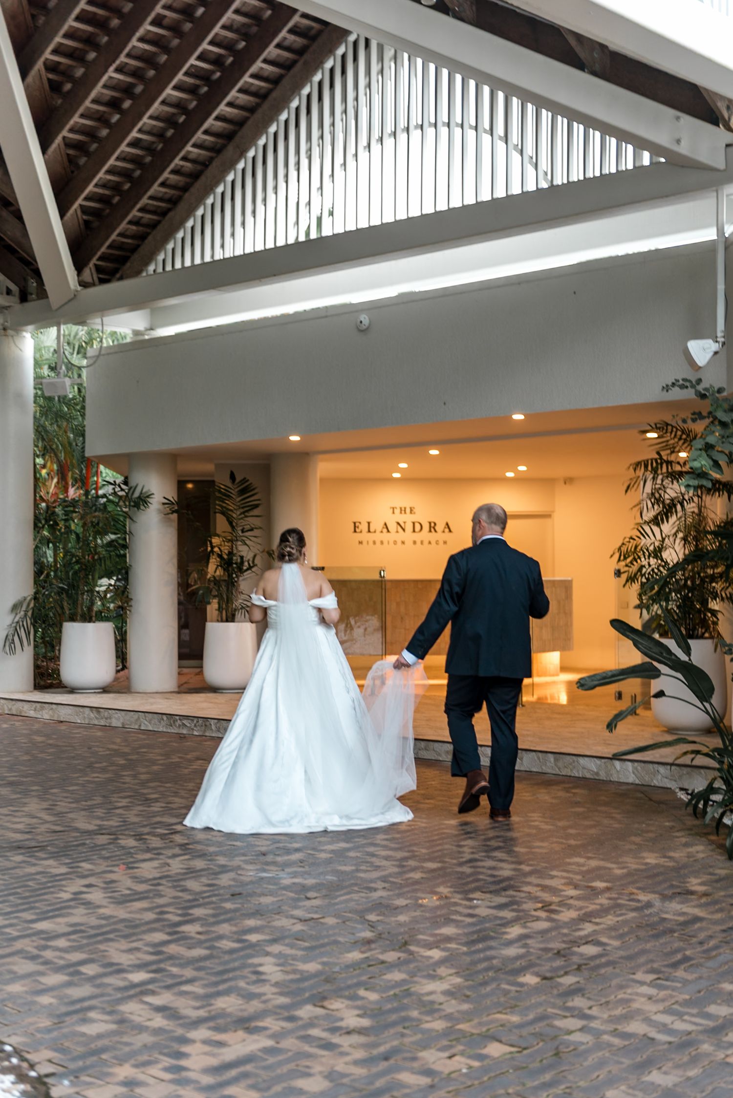 Bride and escort walking hand in hand toward The Elandra wedding venue entrance.