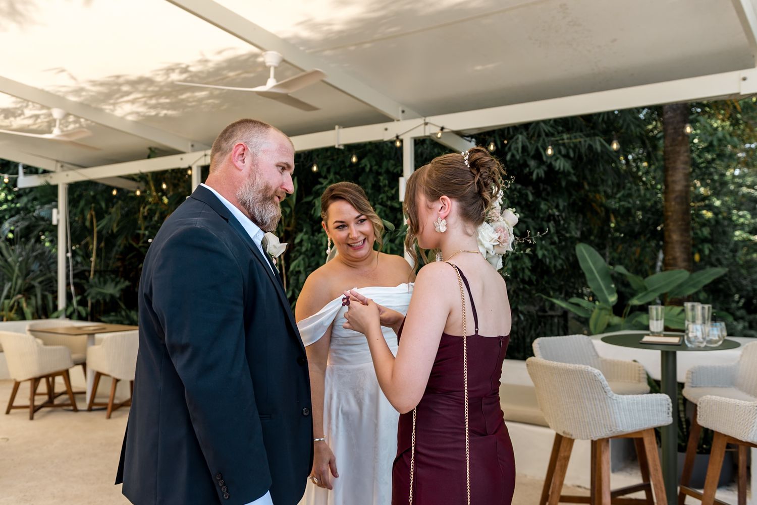 Groom in navy suit shares moment with two guests at elegant outdoor wedding reception.