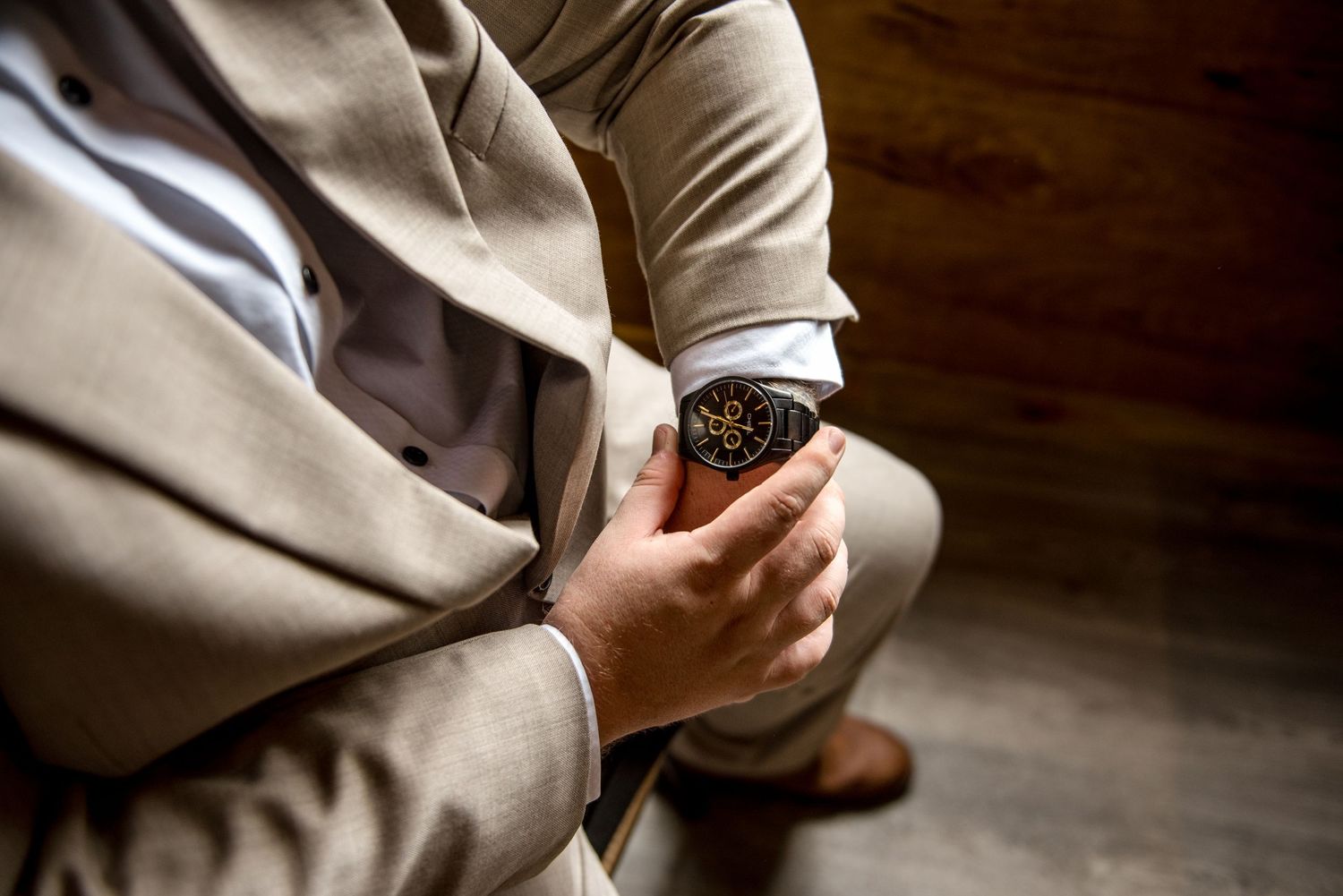 Close-up of groom in beige suit adjusting ornate black and gold watch on wedding day.