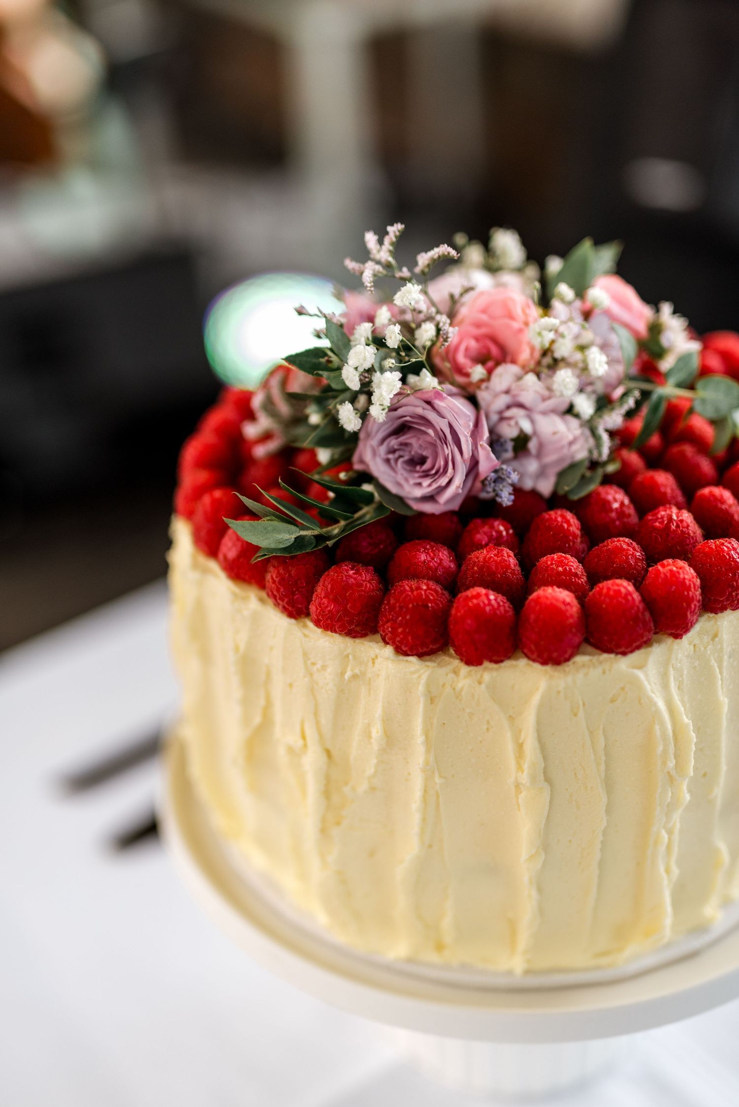 Close-up of white frosted wedding cake decorated with fresh raspberries and pink and purple flowers.