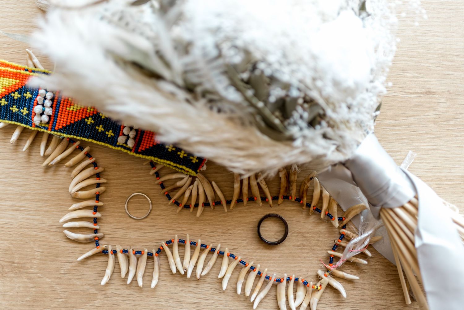 Wedding rings resting on a beaded necklace beside a feathered bouquet and colorful Native accessories.