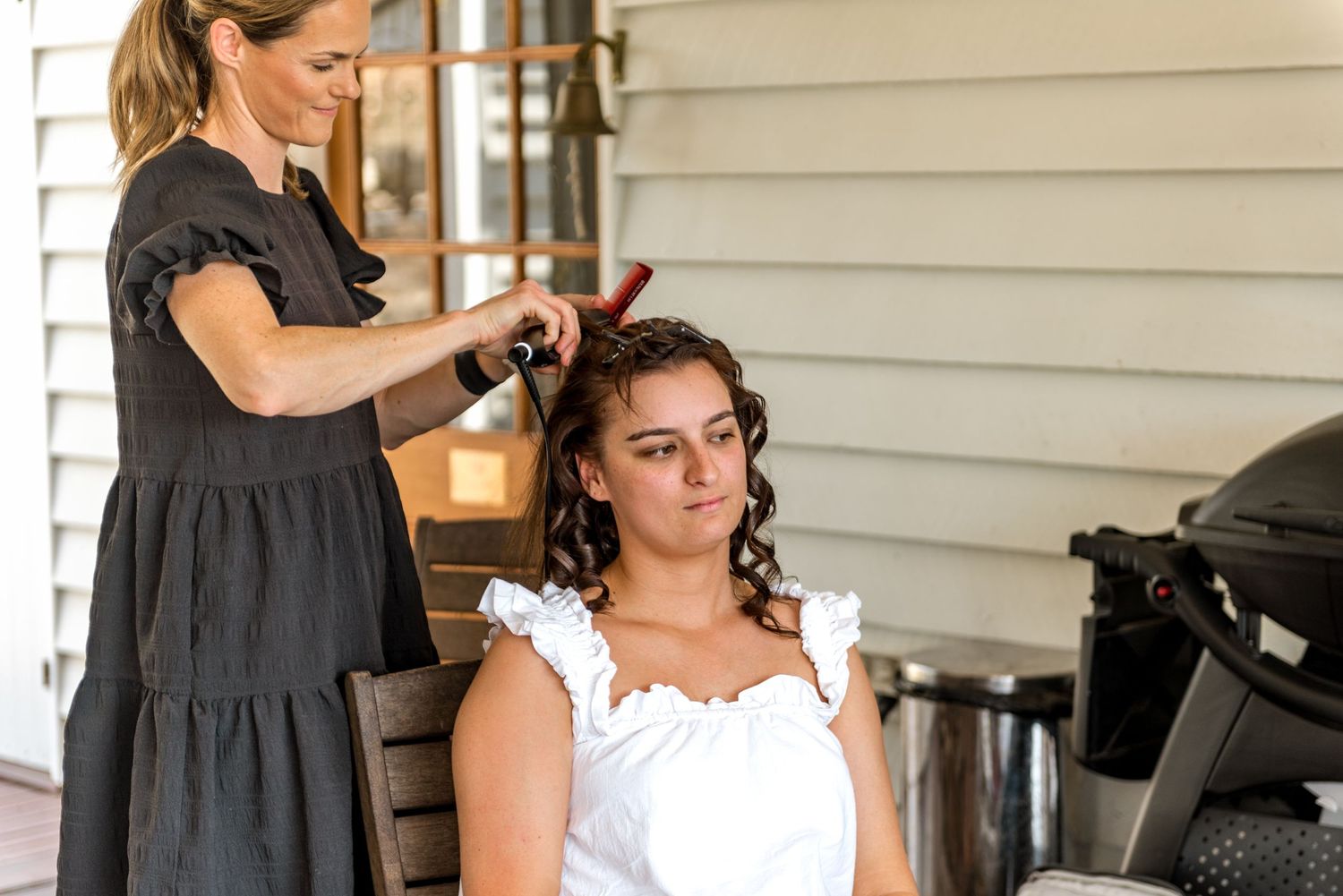 Professional hairstylist styling brides curly hair on a sunny outdoor verandah.