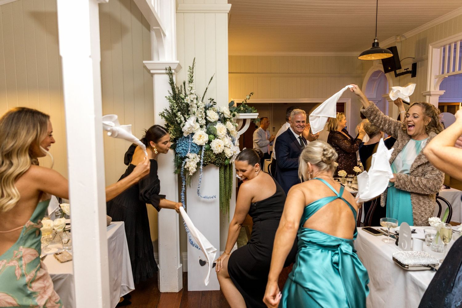 Excited wedding guests waving napkins in celebration at an elegant indoor reception venue.