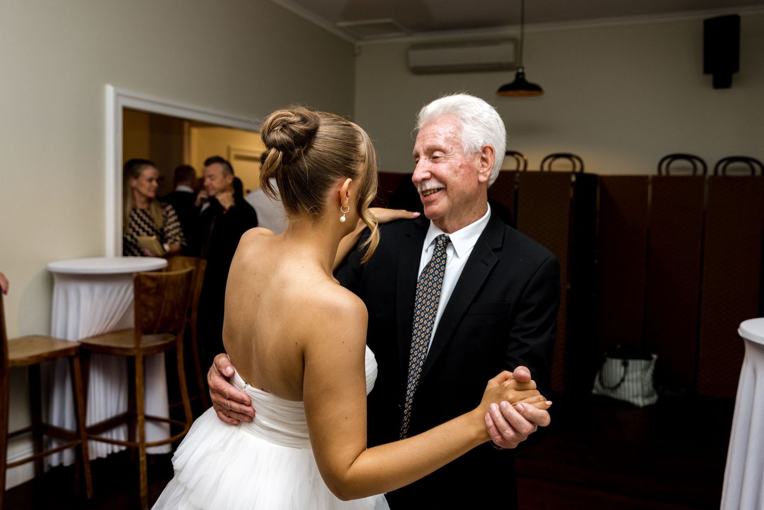 Bride in white gown sharing a father-daughter dance at her wedding reception.