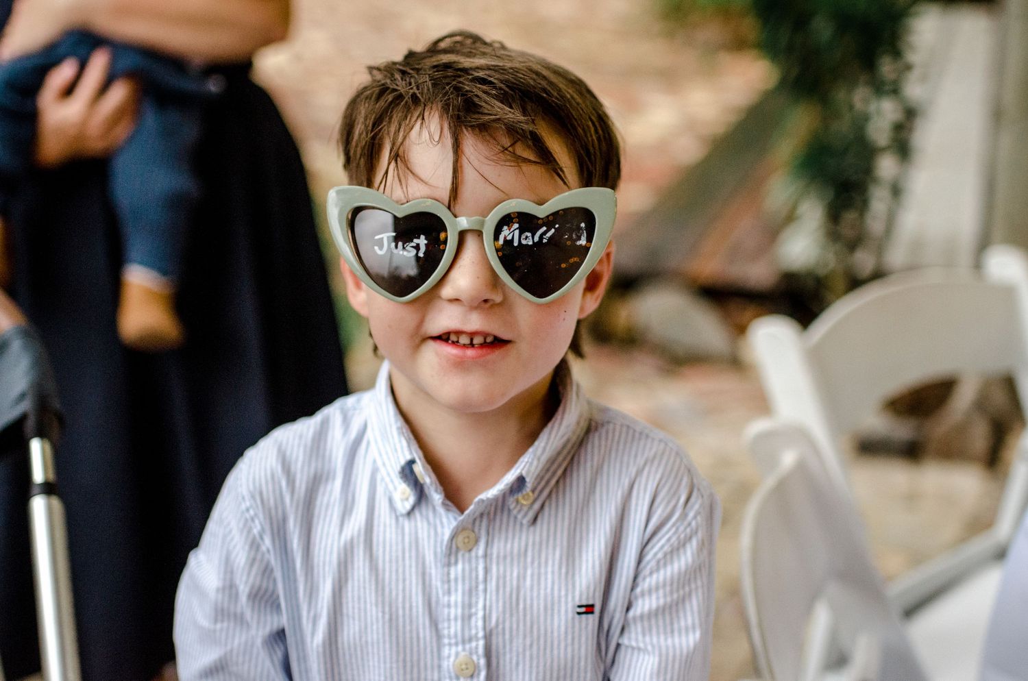 Young boy wearing heart-shaped sunglasses with Mr and Mrs text smiles at wedding celebration.