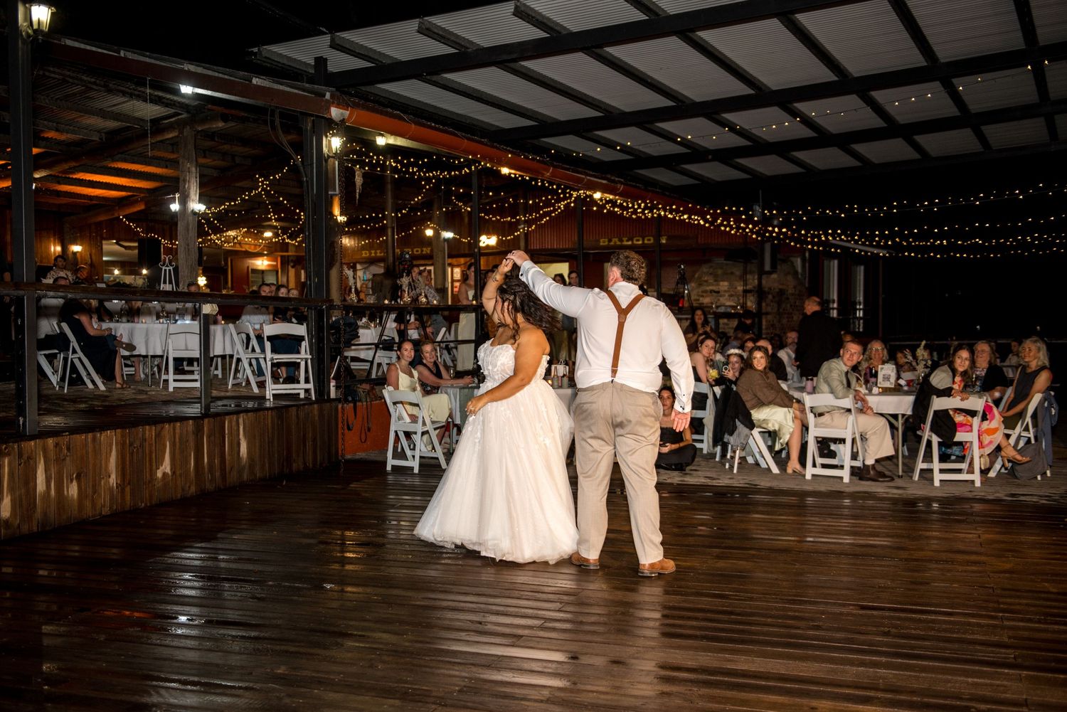 Bride and groom share their first dance on a wooden floor at an outdoor evening wedding reception.