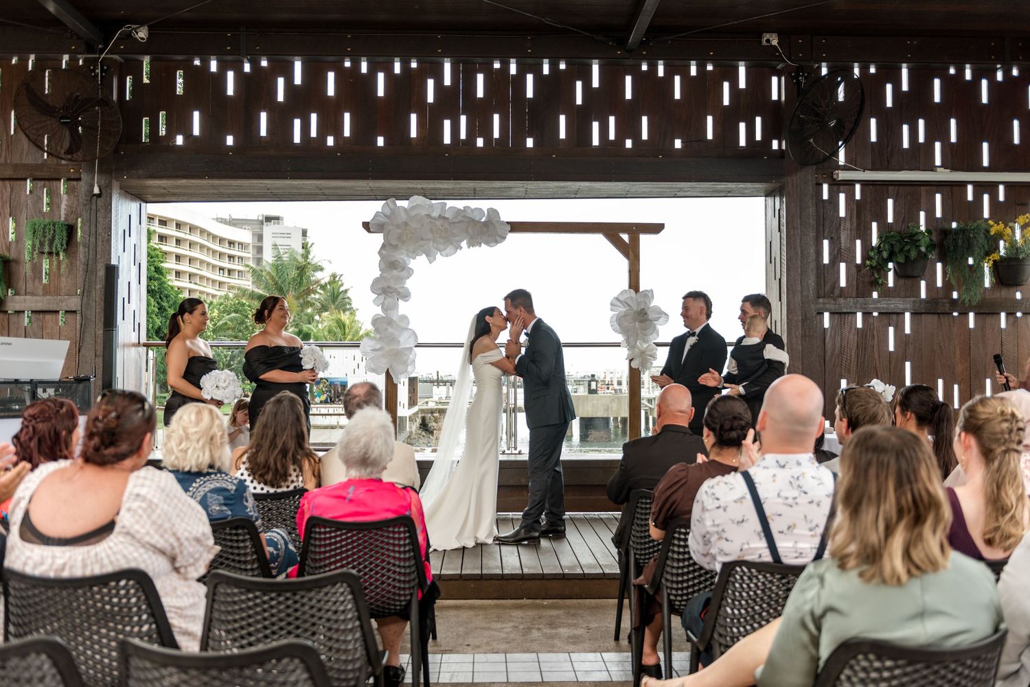 Bride and groom share first kiss at altar before seated wedding guests in decorated venue.
