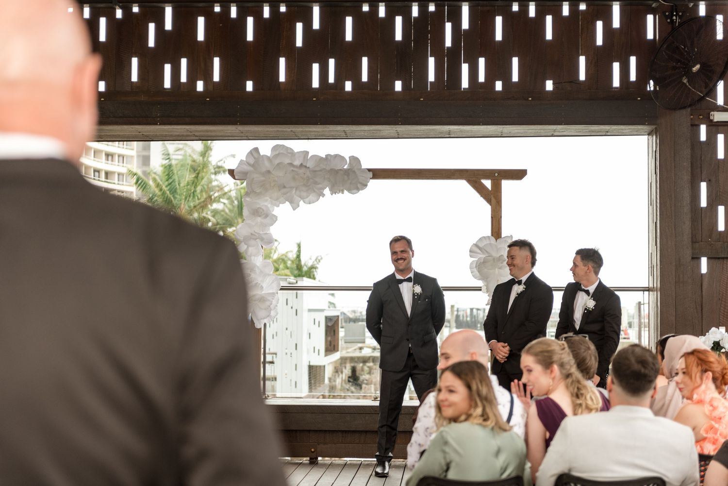 Emotional groom in tuxedo awaits bride at outdoor wedding ceremony altar.