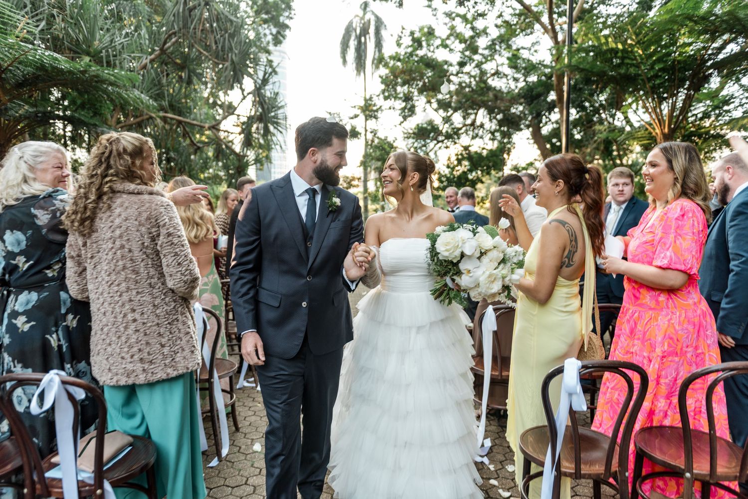 Bride and groom pause on the aisle to greet guests at their lush outdoor garden wedding ceremony.