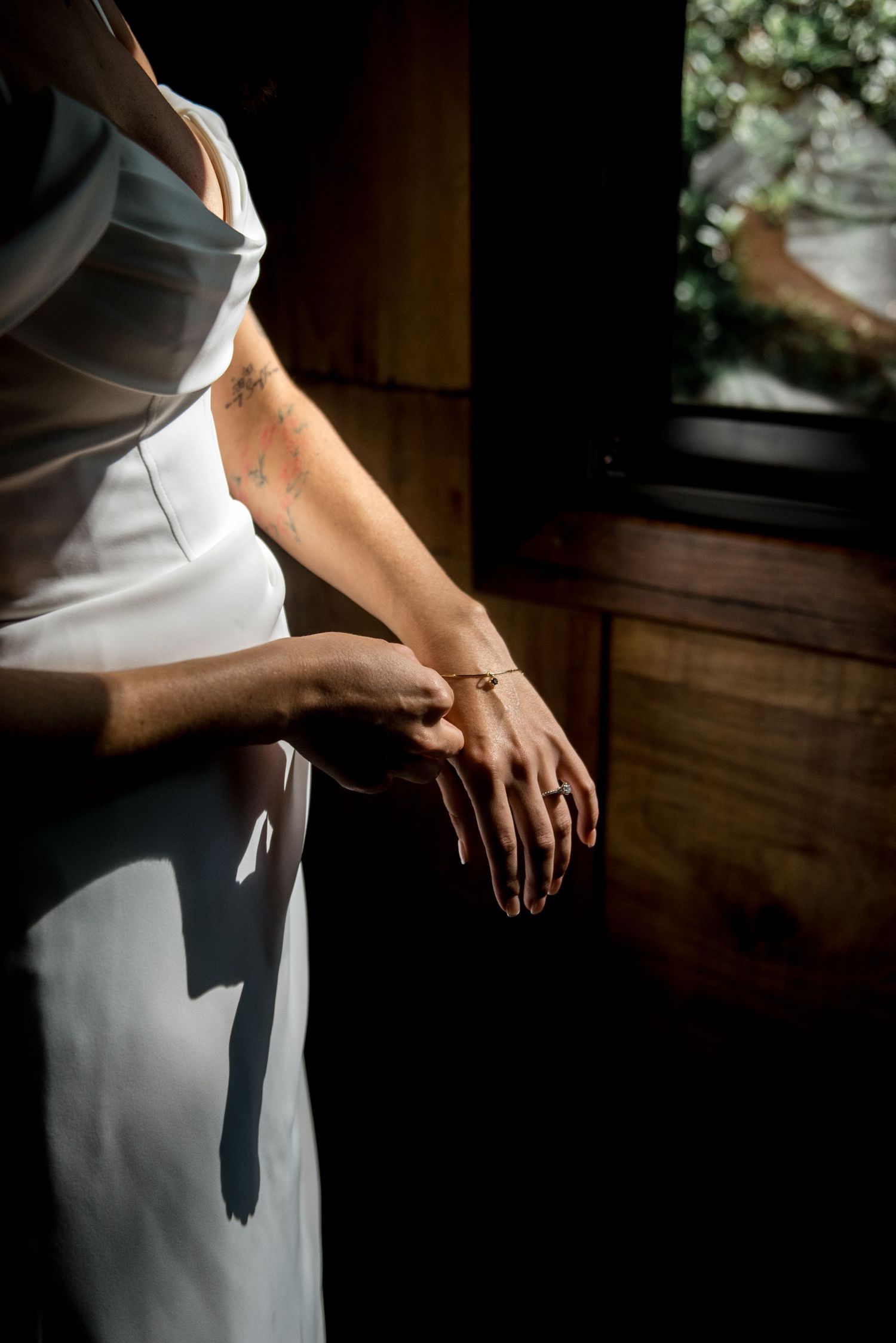 Close-up of bride in white dress adjusting gold bracelet with tattoo visible on wrist.