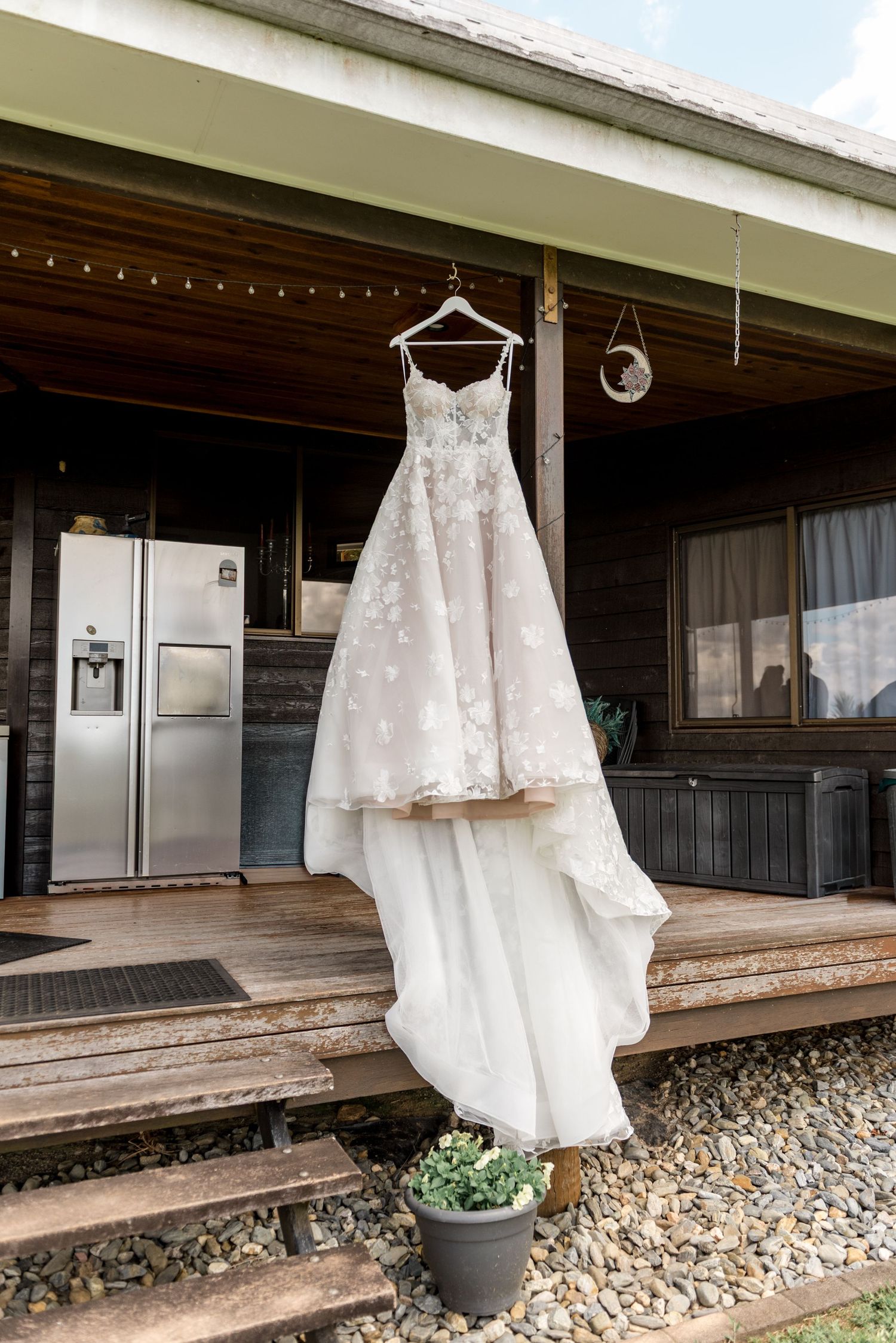 Floral lace wedding dress hanging on a hanger on a rustic wooden porch with mountain views.