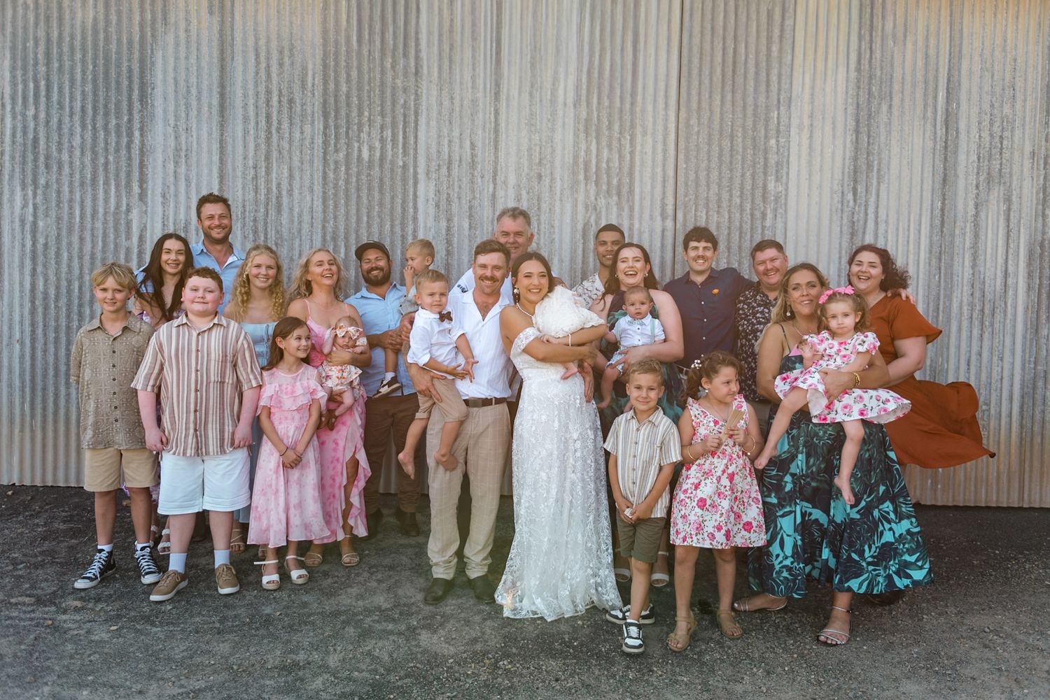 Wedding family portrait with bride, groom, children and relatives posing outside a corrugated barn.