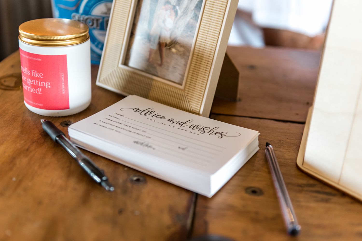 Advice and wishes card pad with pens beside a gold frame and red candle on a wooden table.