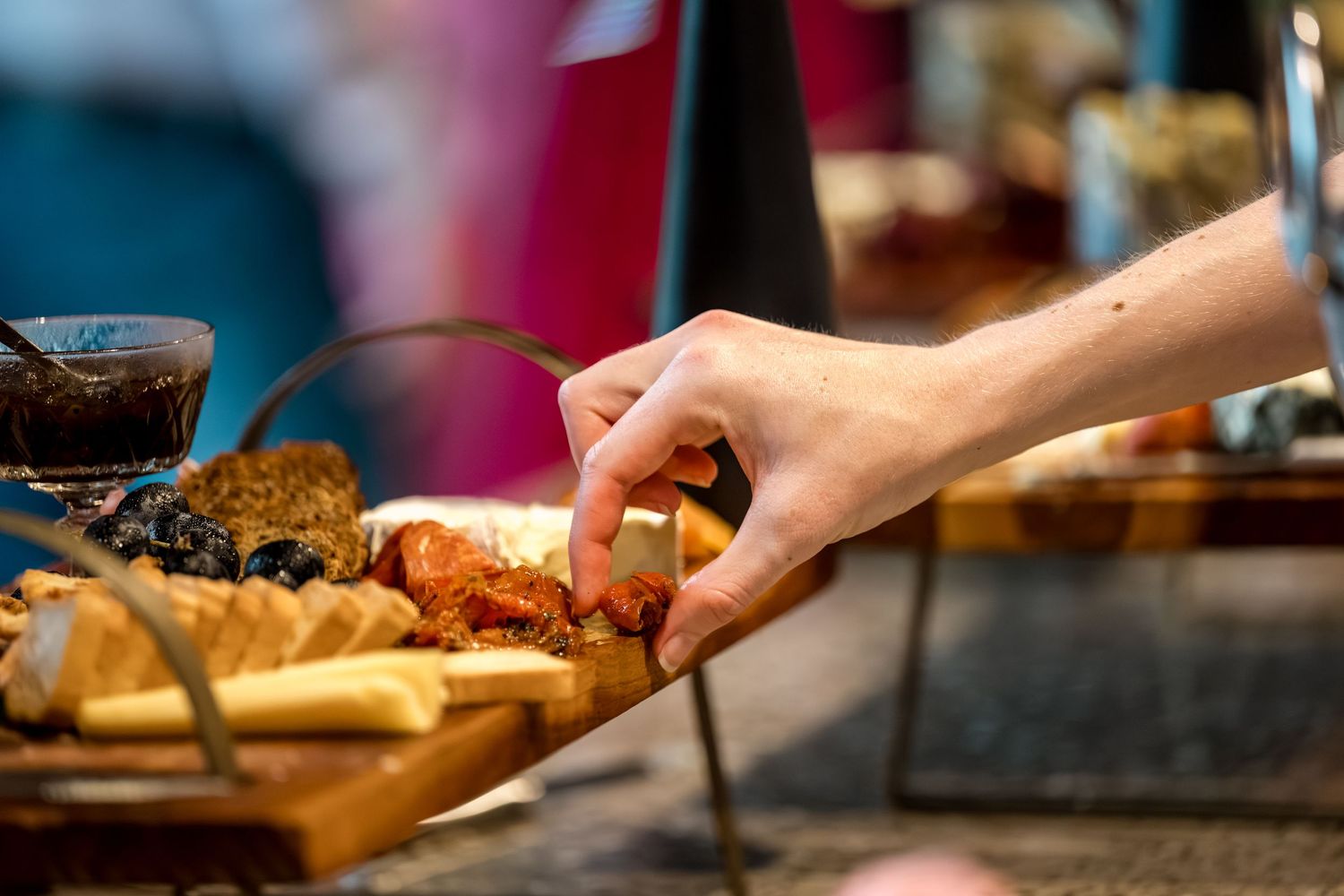 Hand reaching for food on a rustic wooden charcuterie board at an event.