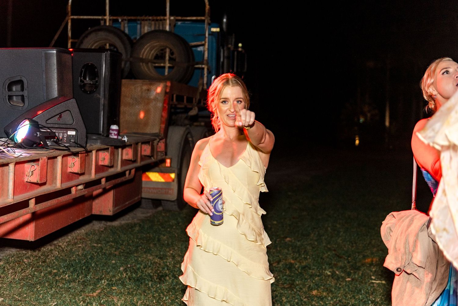 Woman in yellow ruffled dress dancing outdoors at a night event holding a drink.