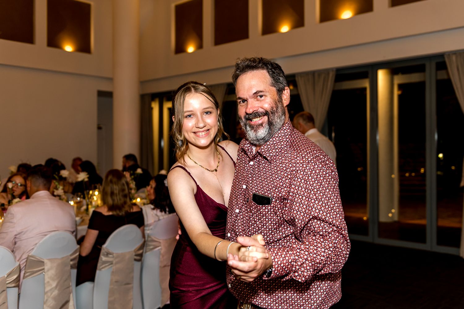 Smiling couple dancing at wedding reception in warmly lit elegant indoor venue.