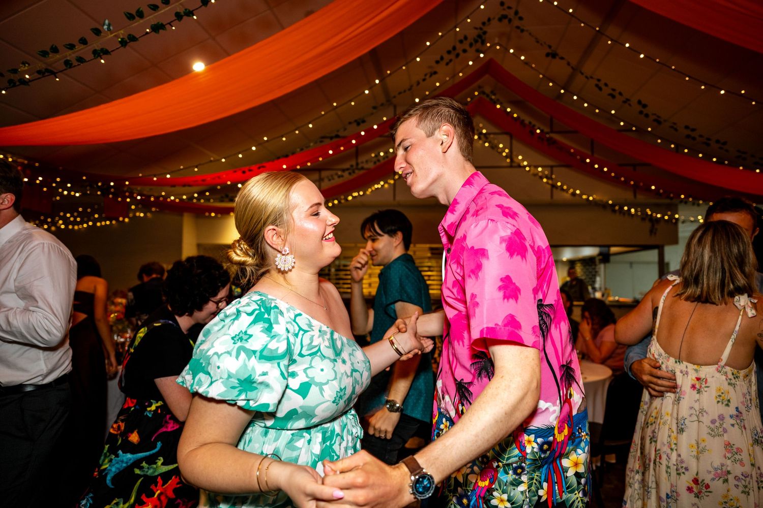 Couple dancing and smiling together at a colorful wedding reception party.