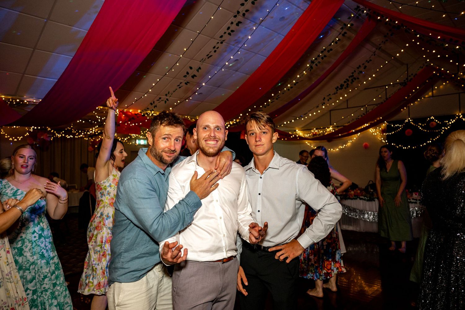 Three men posing and smiling together on the dance floor at a wedding.