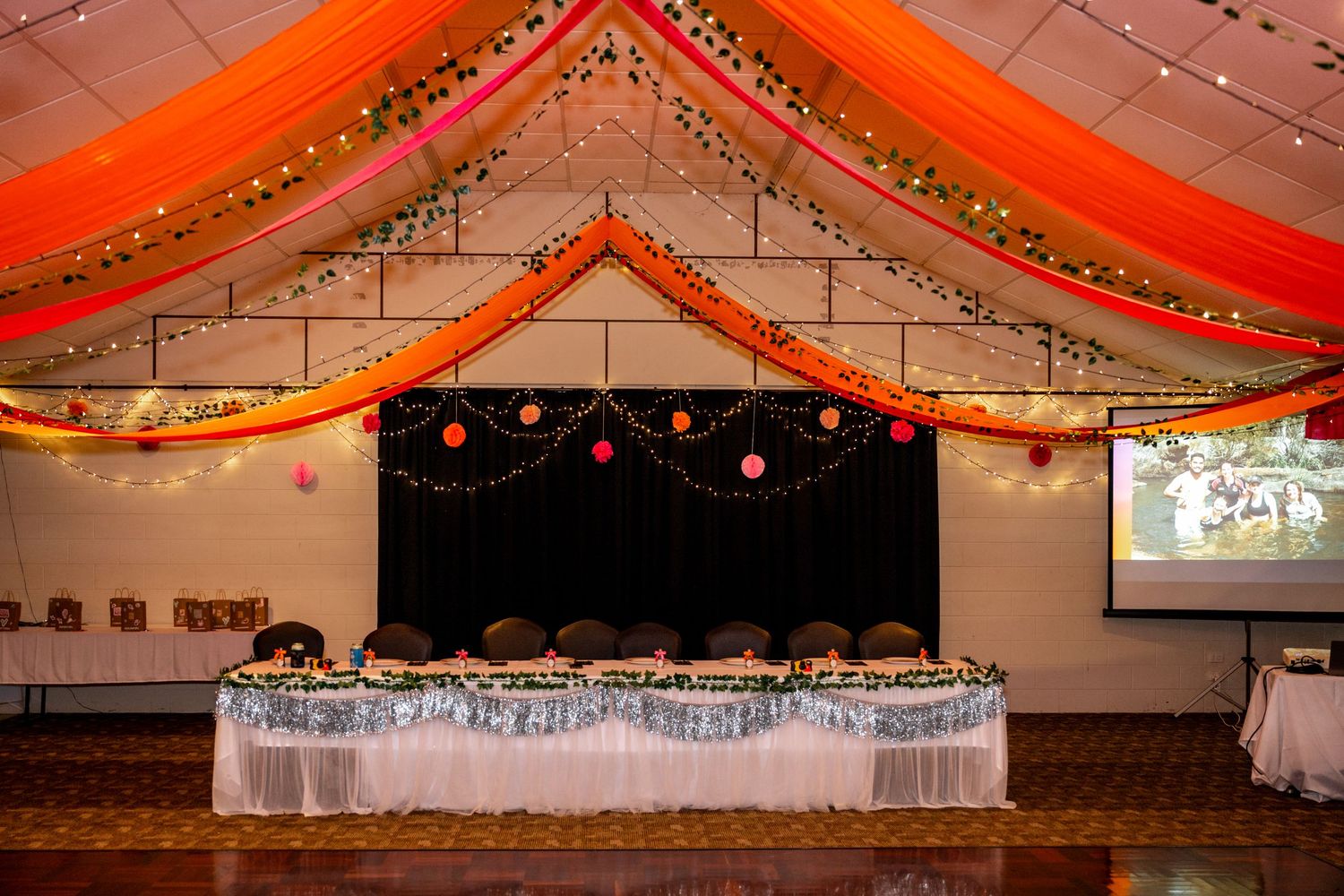 Elegant wedding reception hall decorated with vibrant orange and red draped fabric ceiling, fairy lights, and colorful paper lanterns.