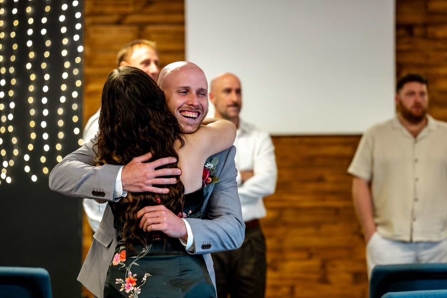 Groom in grey suit warmly hugging a guest at the wedding reception venue.