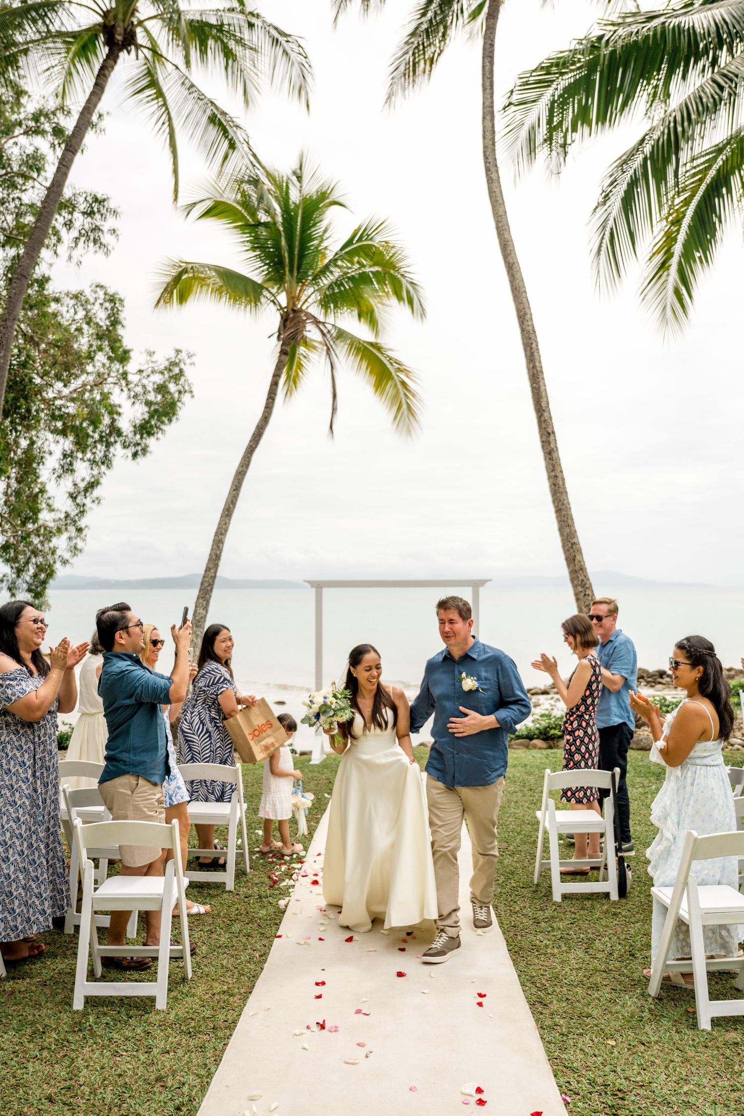 Newlyweds walking down the aisle at a tropical beachside wedding as guests applaud at Little Cove, Port Douglas.