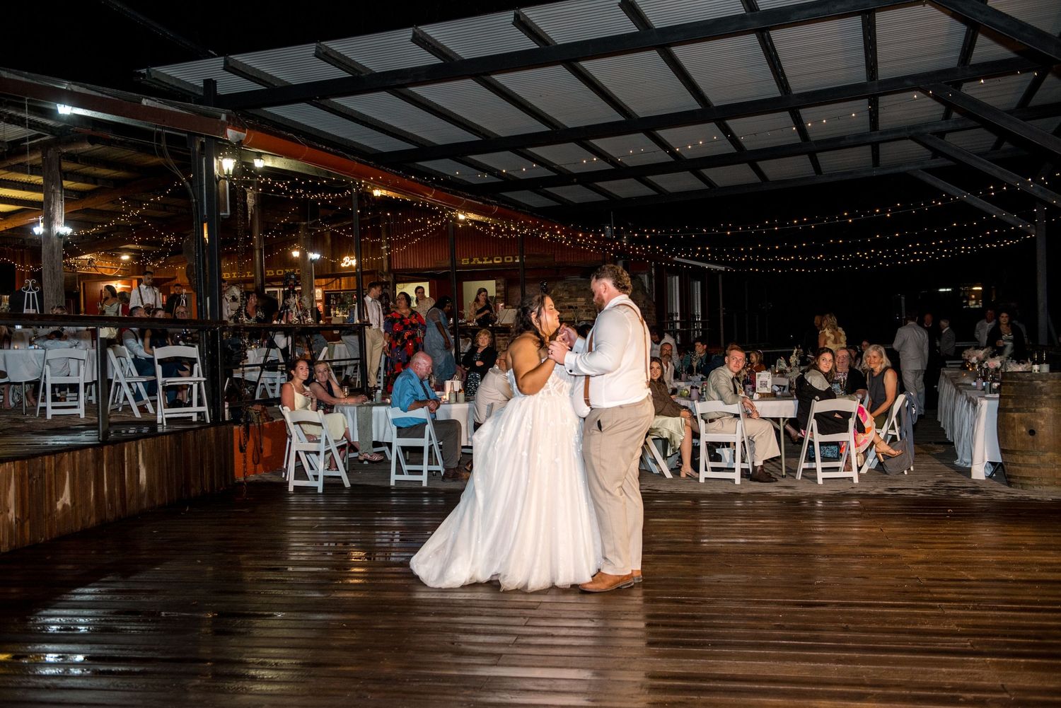 Bride and groom dancing together at their outdoor wedding reception with guests watching nearby.