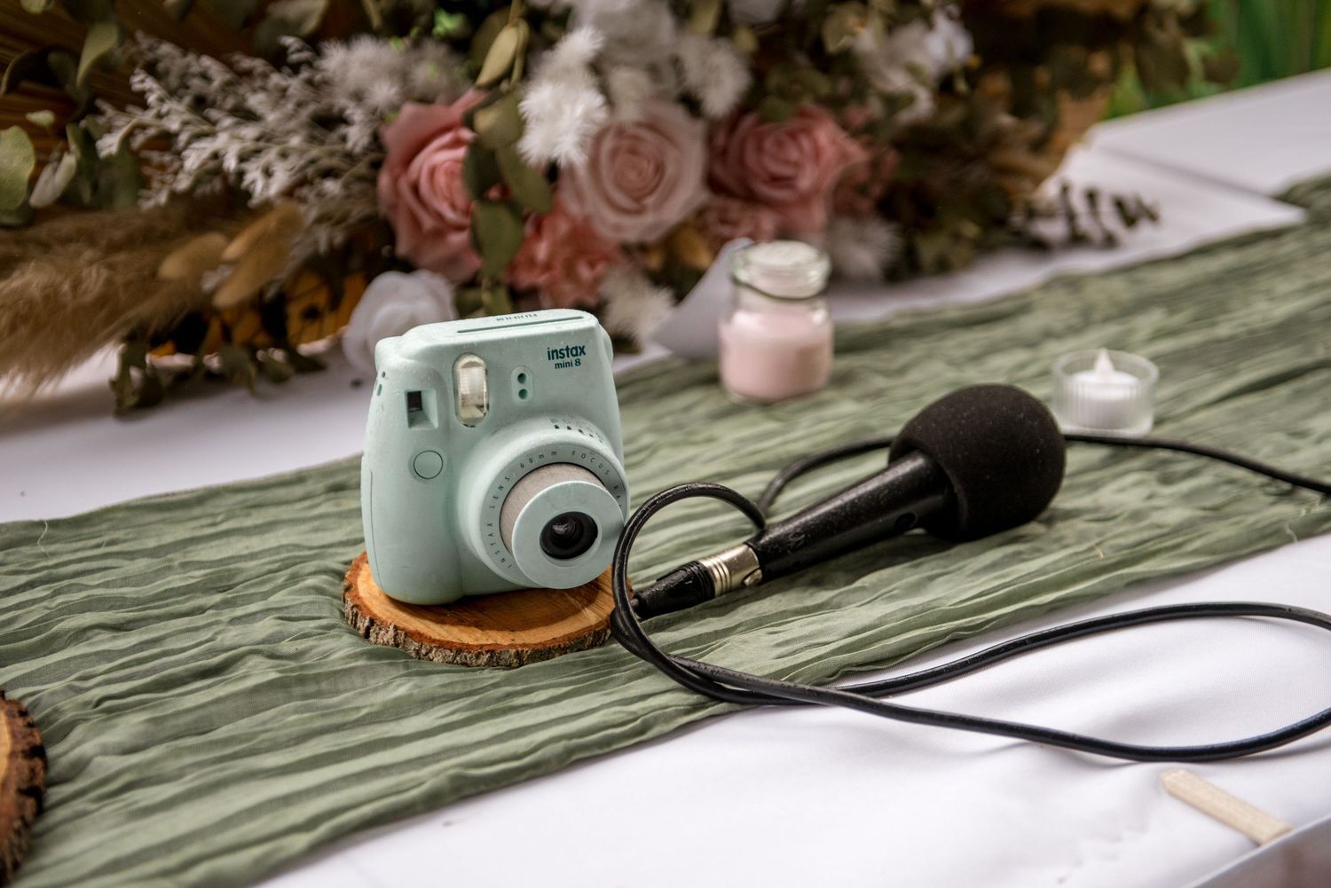 Mint green Fujifilm Instax mini camera and microphone on a green table runner at a wedding.