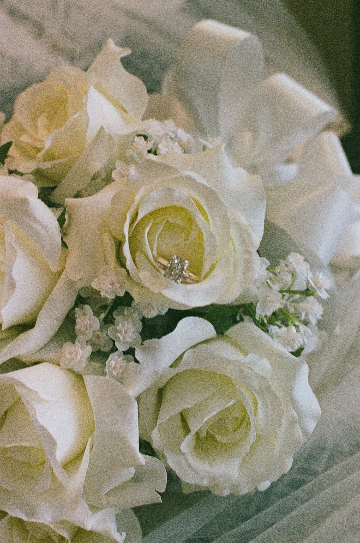Diamond engagement ring nestled in a bouquet of white roses and baby's breath for a wedding.