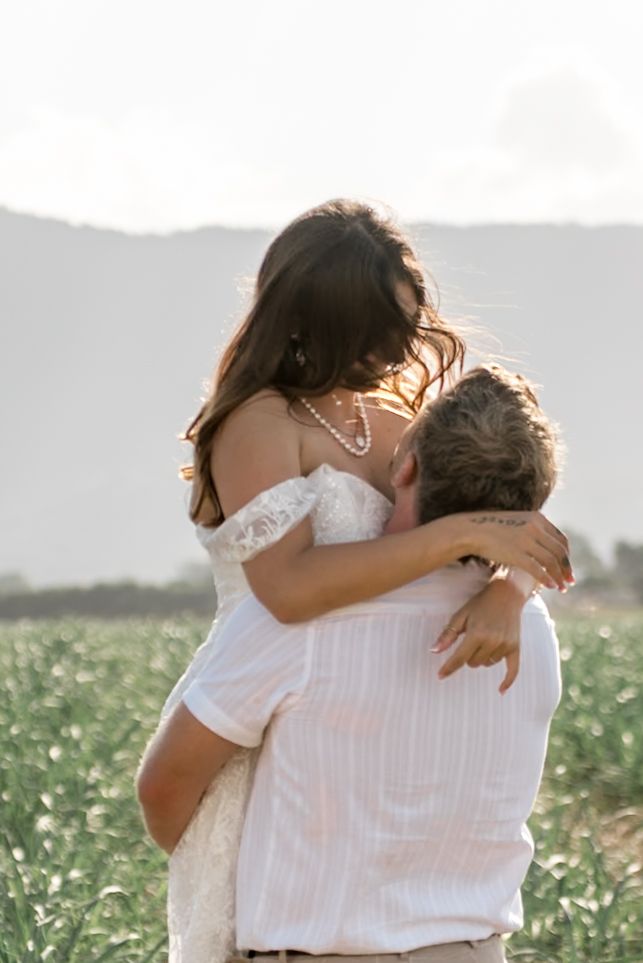 Groom lifting bride in white lace wedding dress in a romantic outdoor field photo session.