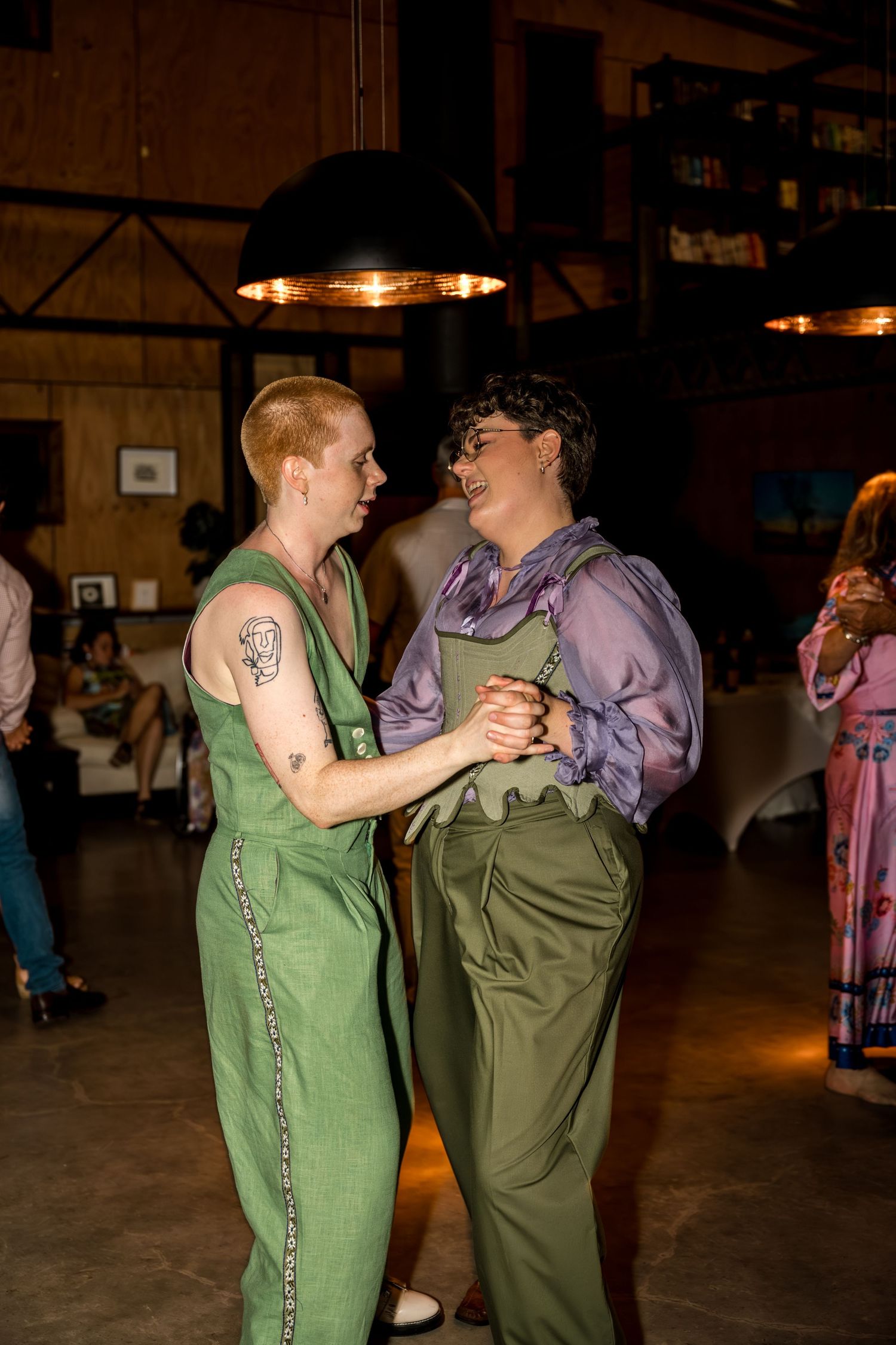 Two newlyweds in green wedding attire gaze lovingly at each other while dancing.