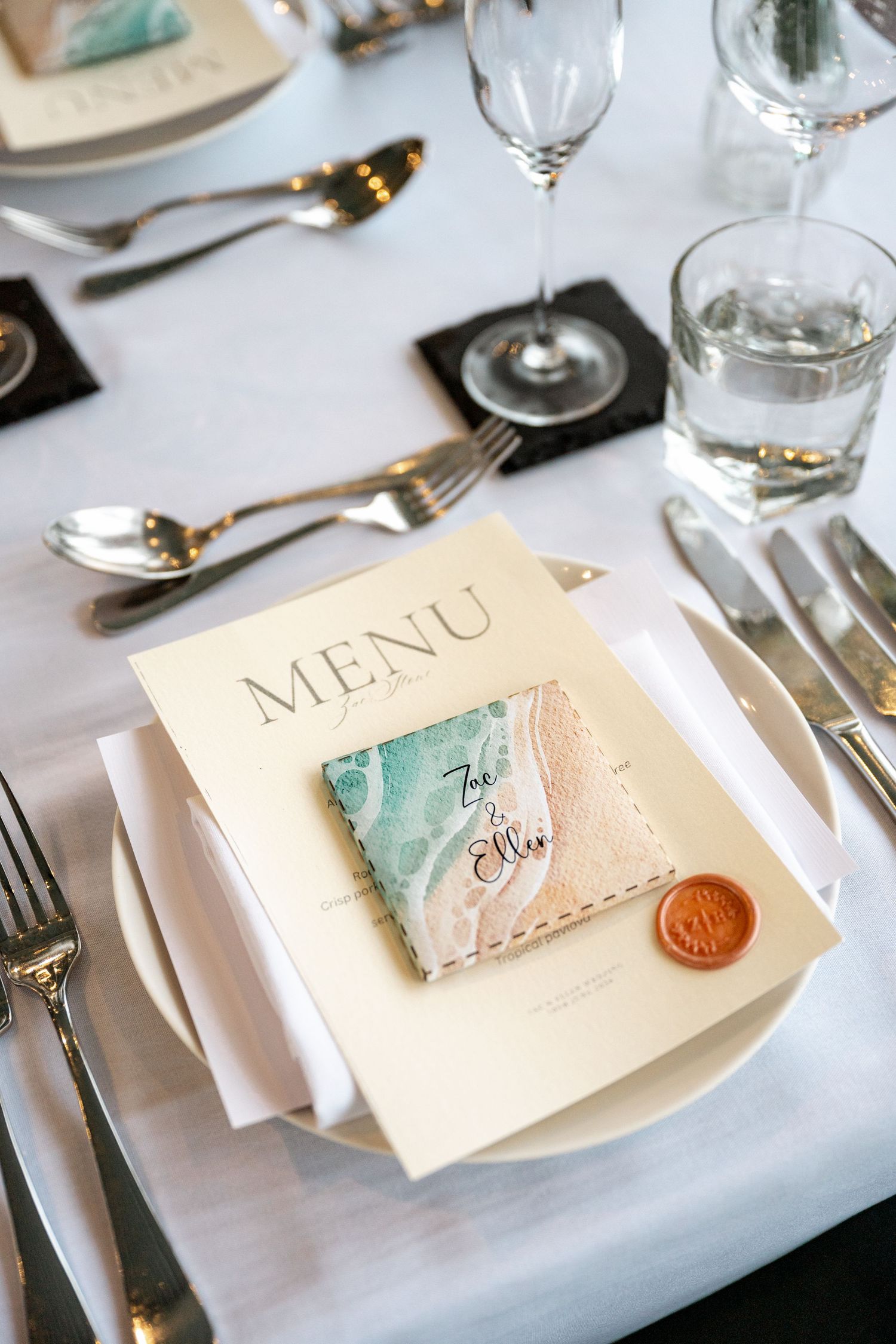 Wedding place setting with menu card, beach-themed name card, and wax seal on white plate at Sheraton Grand Mirage Port Douglas.