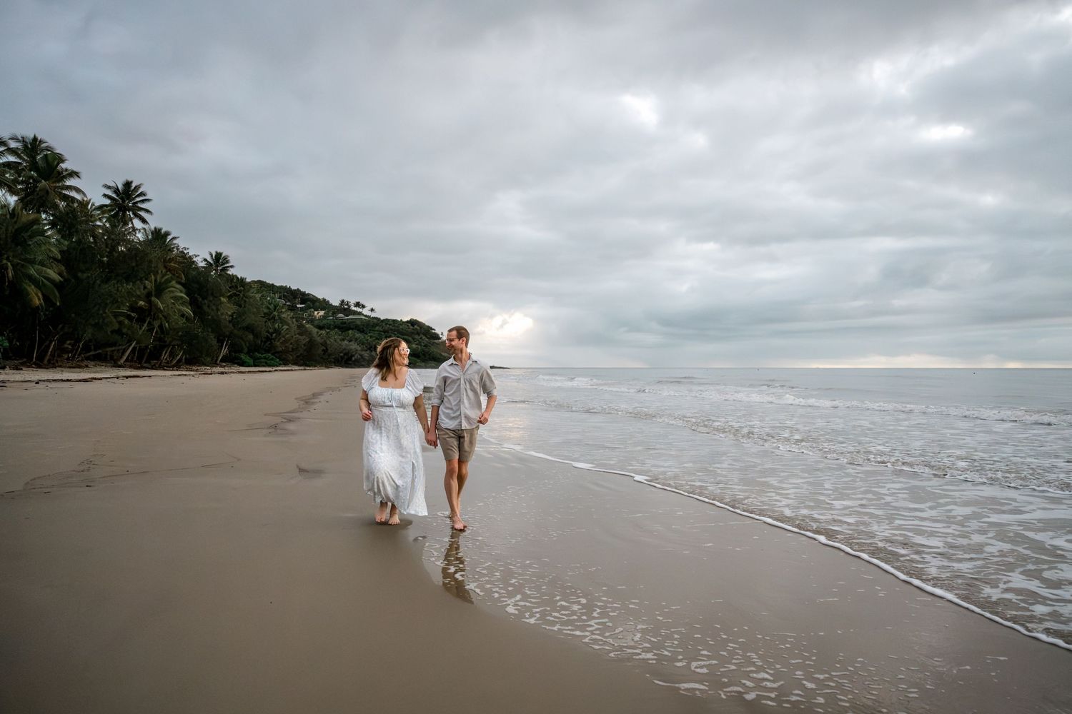 Happy couple holding hands and walking barefoot along a scenic tropical beach at sunset at Four Mile Beach, Port Douglas.