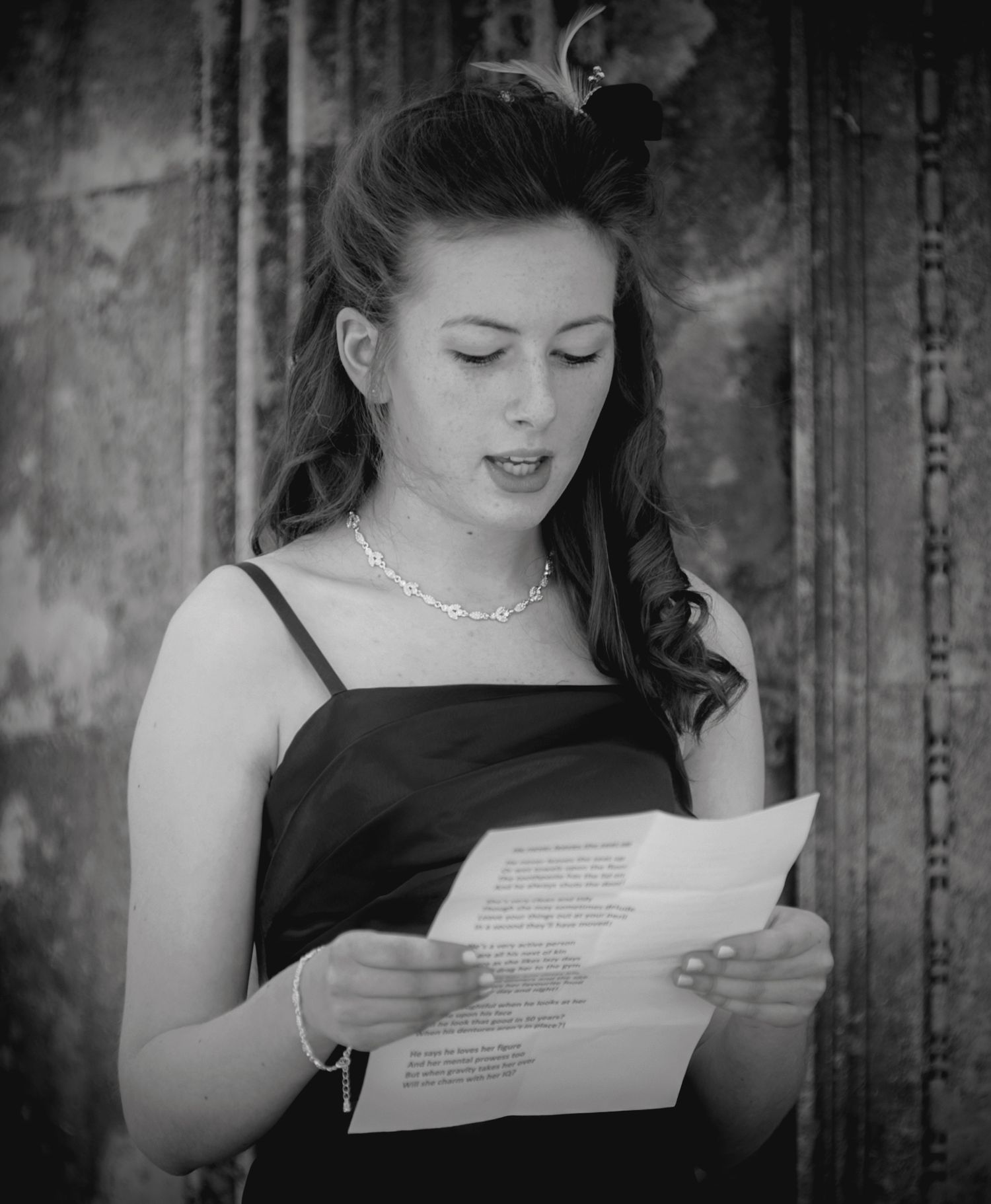 Black and white photograph of a bridesmaid in a thin strap dress reading a wedding speech or reading from a paper.