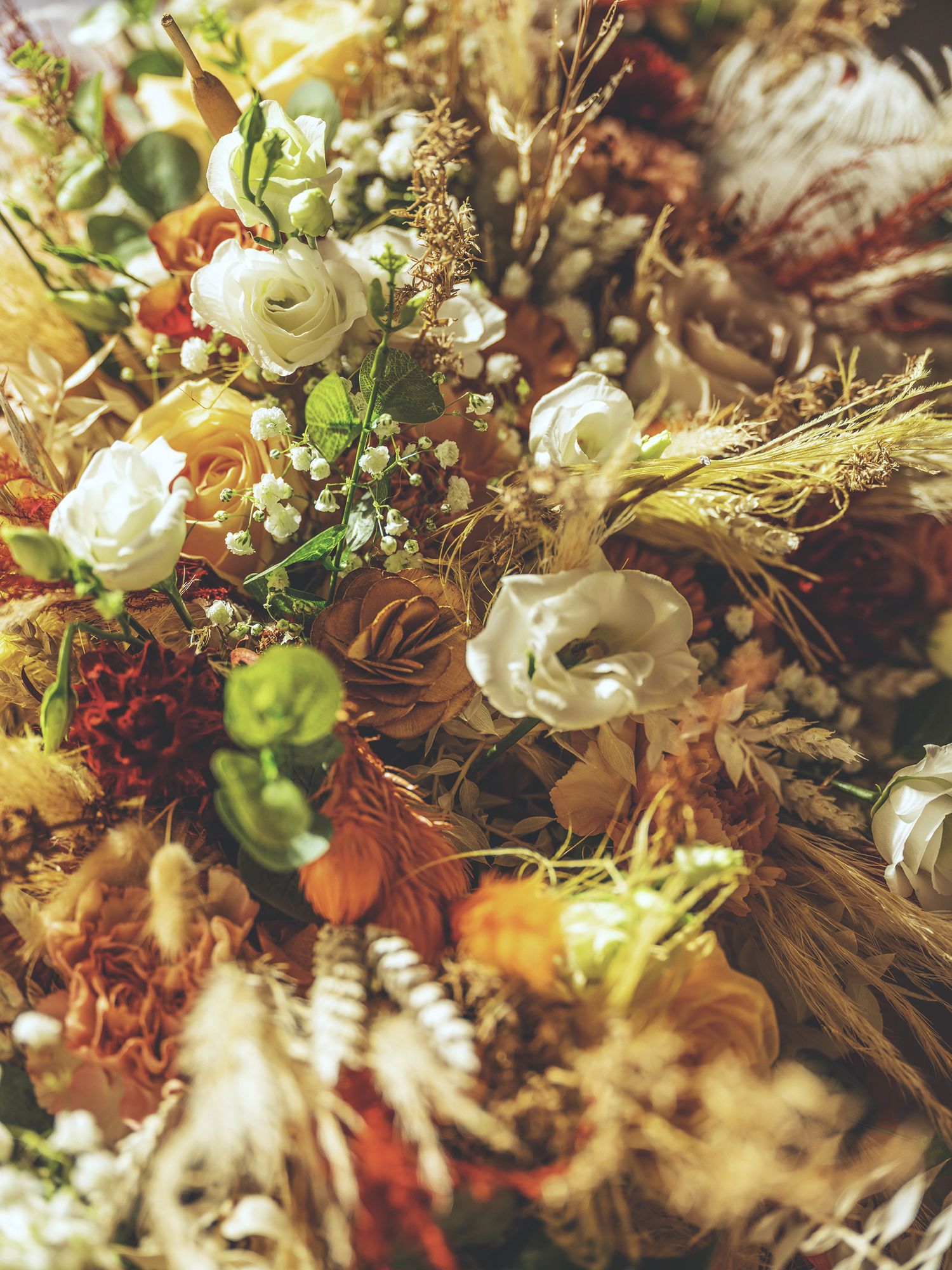 Close-up texture photograph of an autumn bridal bouquet with white eustoma, dried wheat grass, and rust roses.