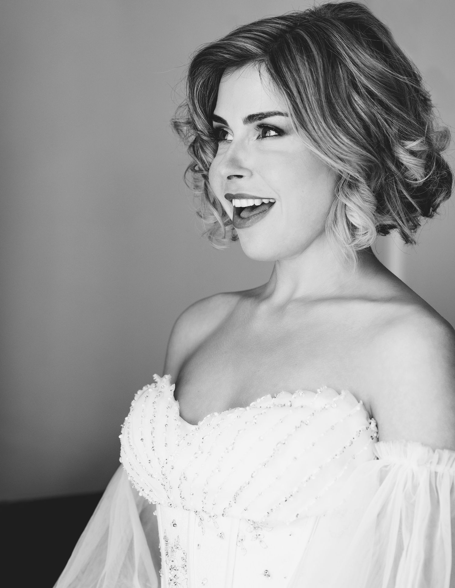 Black and white profile portrait of a smiling bride in a strapless beaded wedding gown with tulle sleeves.