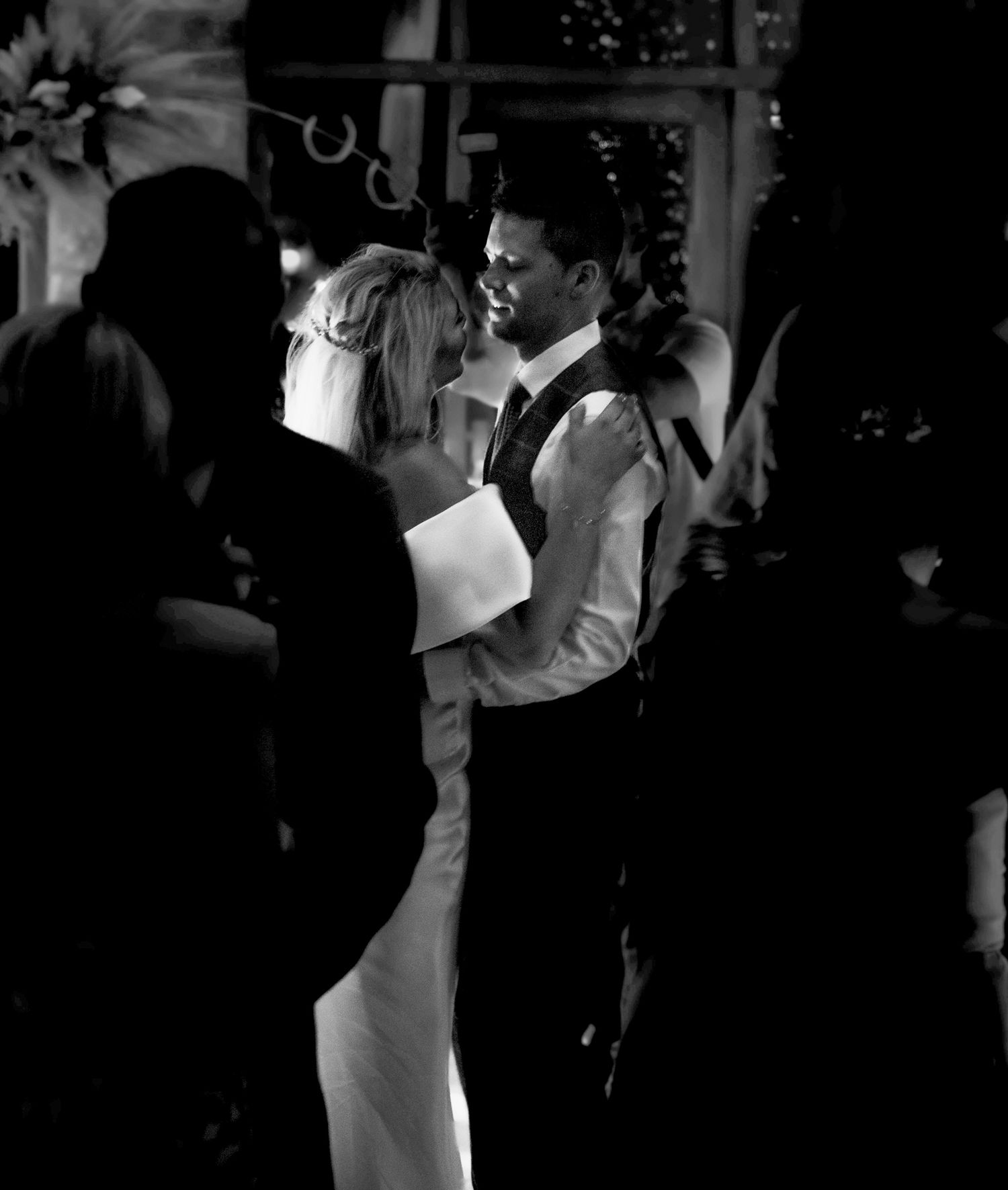 Black and white candid photograph of a bride and groom during their first dance, surrounded by wedding guests.
