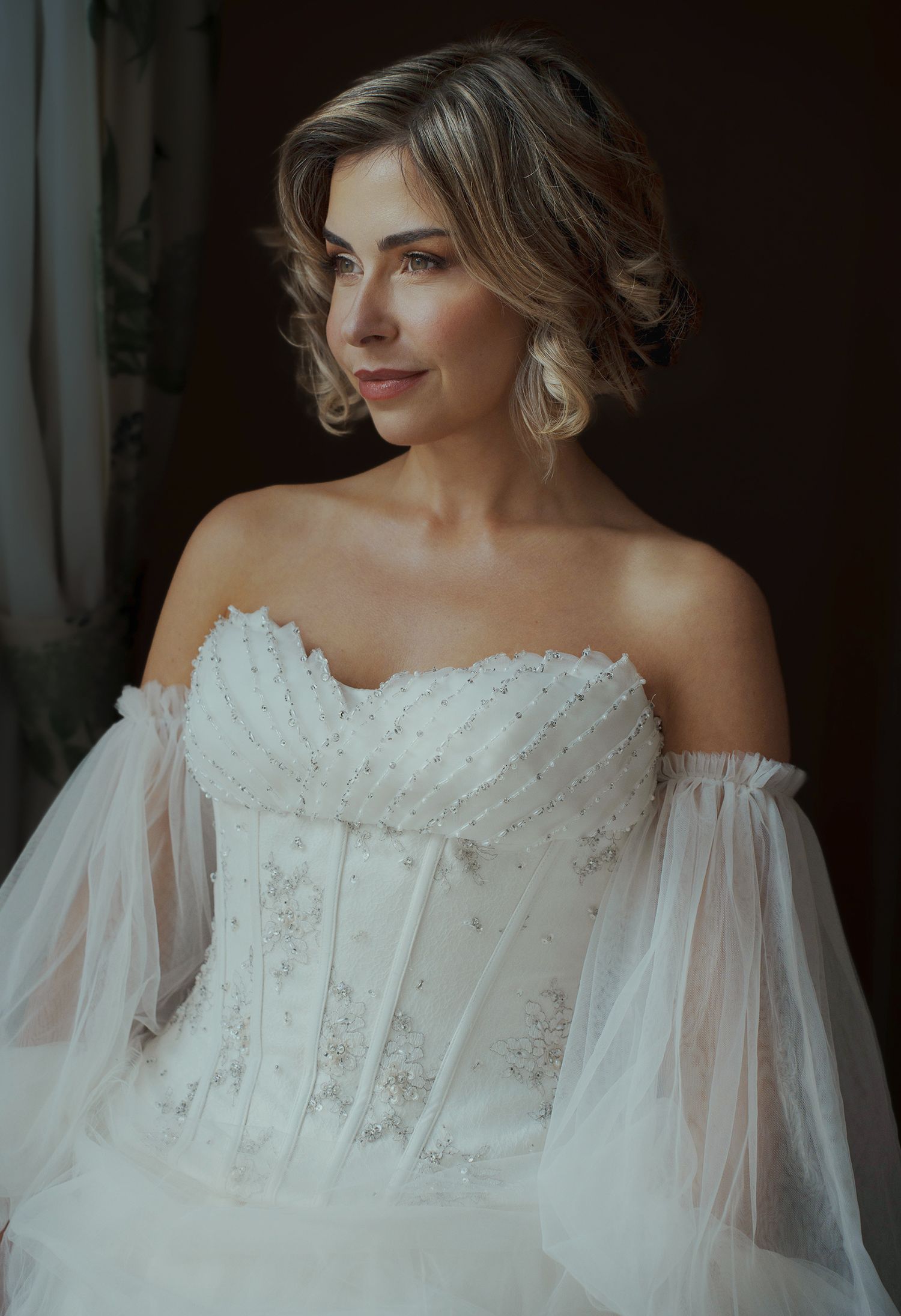 Editorial bridal portrait in a beaded corset bodice wedding dress with detached off-the-shoulder tulle sleeves.