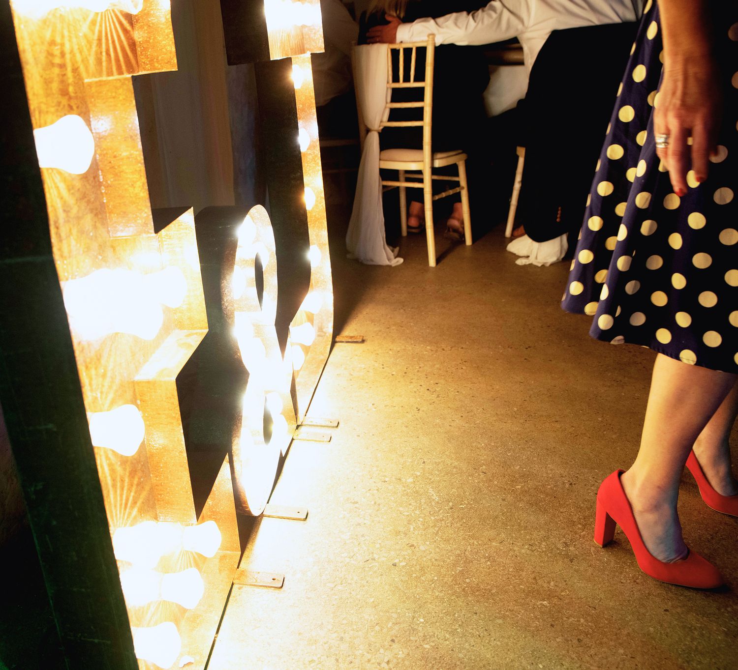 Low angle detail shot of large light up letters on a dance floor next to a guest in a polka dot dress and red heels.