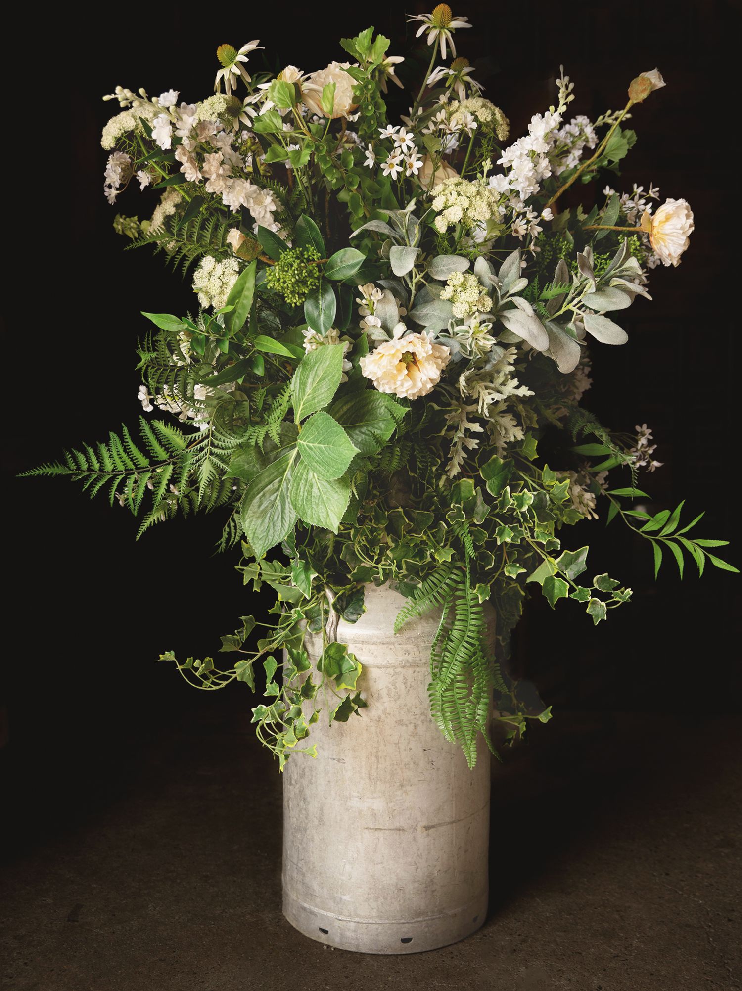 Rustic wedding floral arrangement with white roses, greenery, and ferns inside an antique metal milk churn.