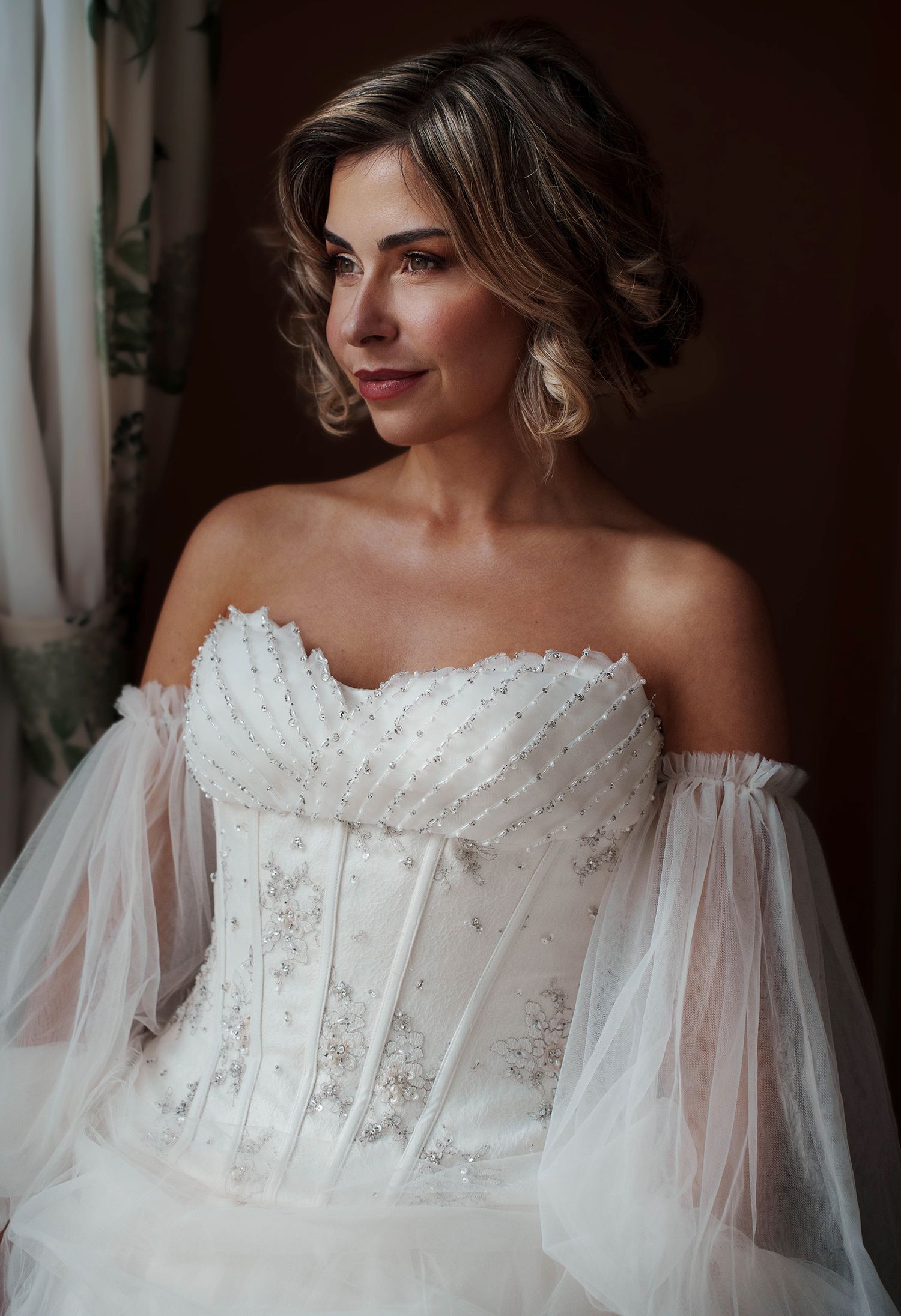 Editorial bridal portrait in a beaded corset bodice wedding dress with detached off-the-shoulder tulle sleeves.