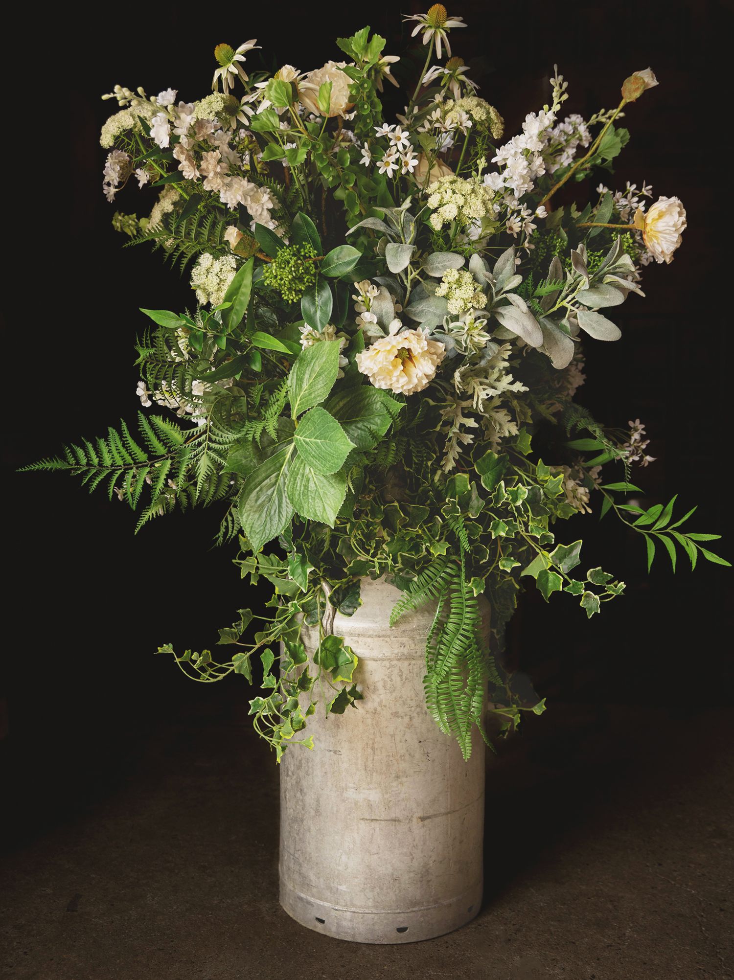 Rustic wedding floral arrangement with white roses, greenery, and ferns inside an antique metal milk churn.
