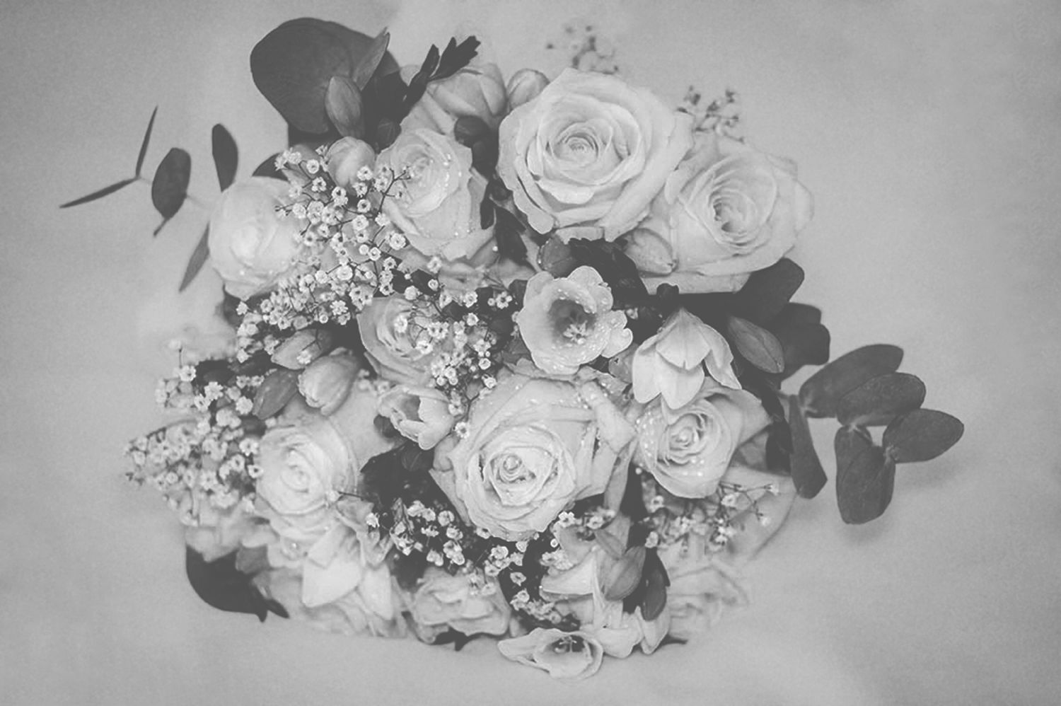Black and white top-down photograph of a wedding bouquet featuring roses, gypsophila, and eucalyptus leaves.