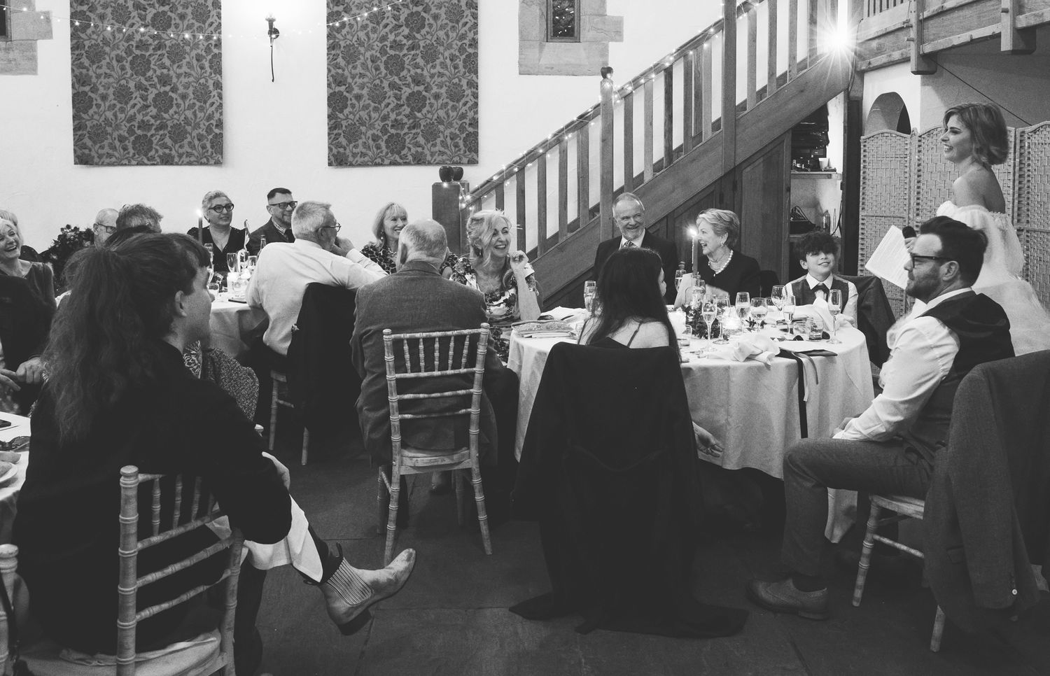 Black and white candid photo of a bride delivering a speech during the wedding breakfast in a rustic barn venue.