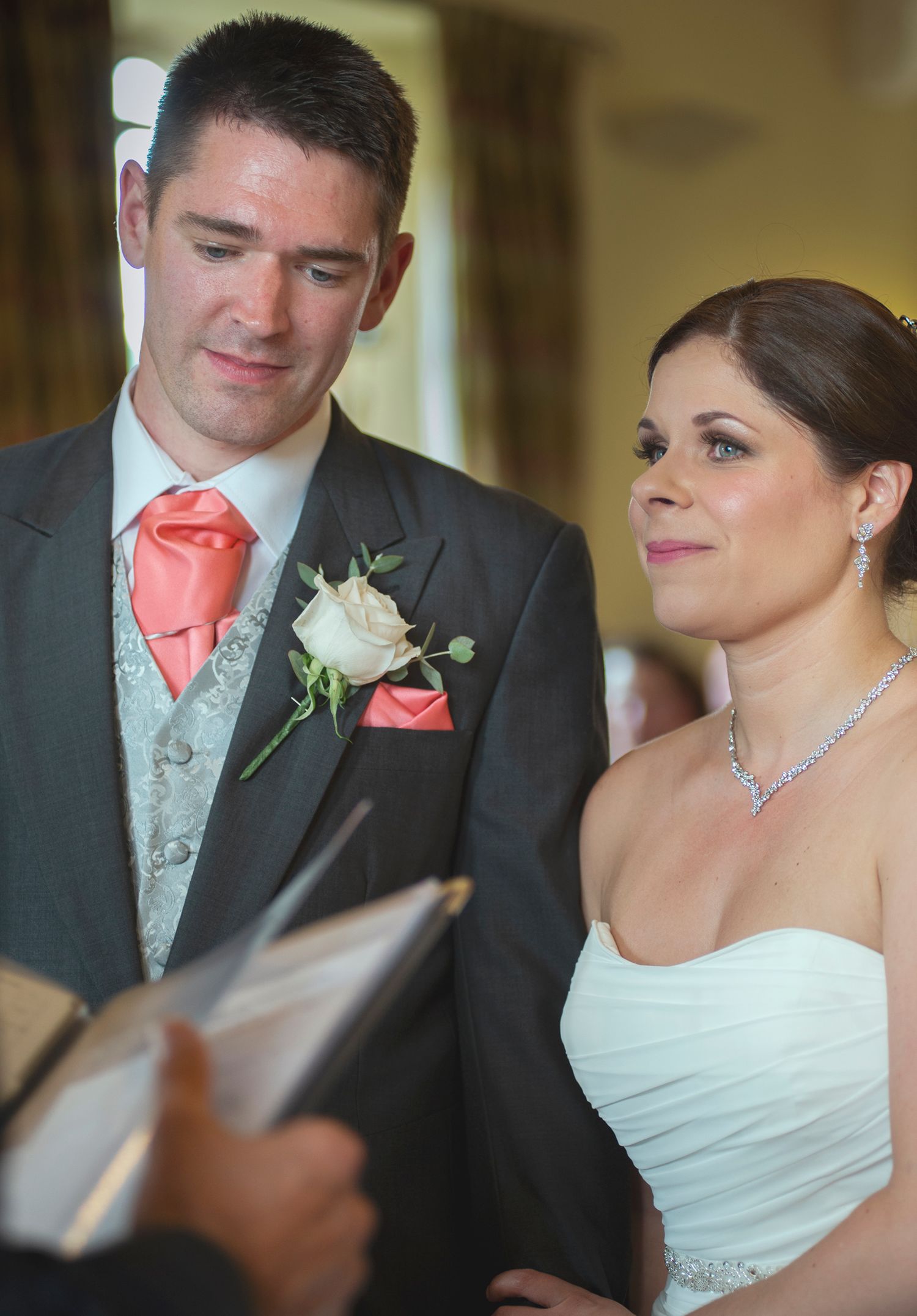 Bride and groom listening during their indoor wedding ceremony, with the celebrant holding a book in the foreground.