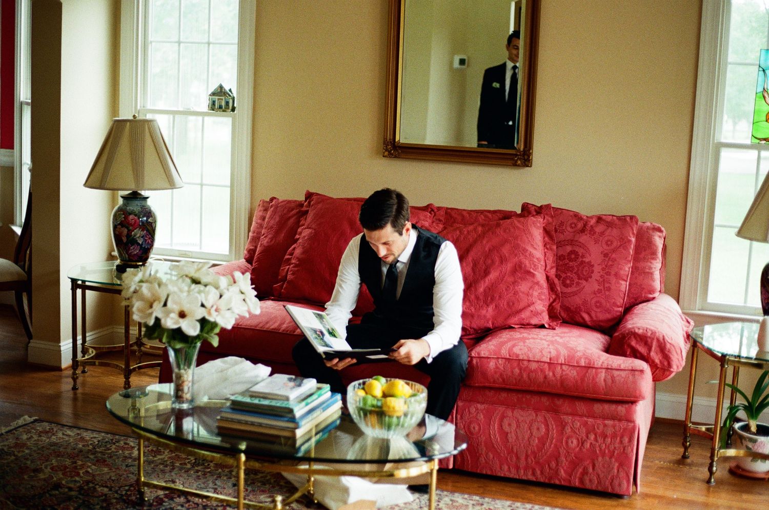 A cozy living room interior features a red leather sofa, hardwood floors, and large windows letting in natural light.