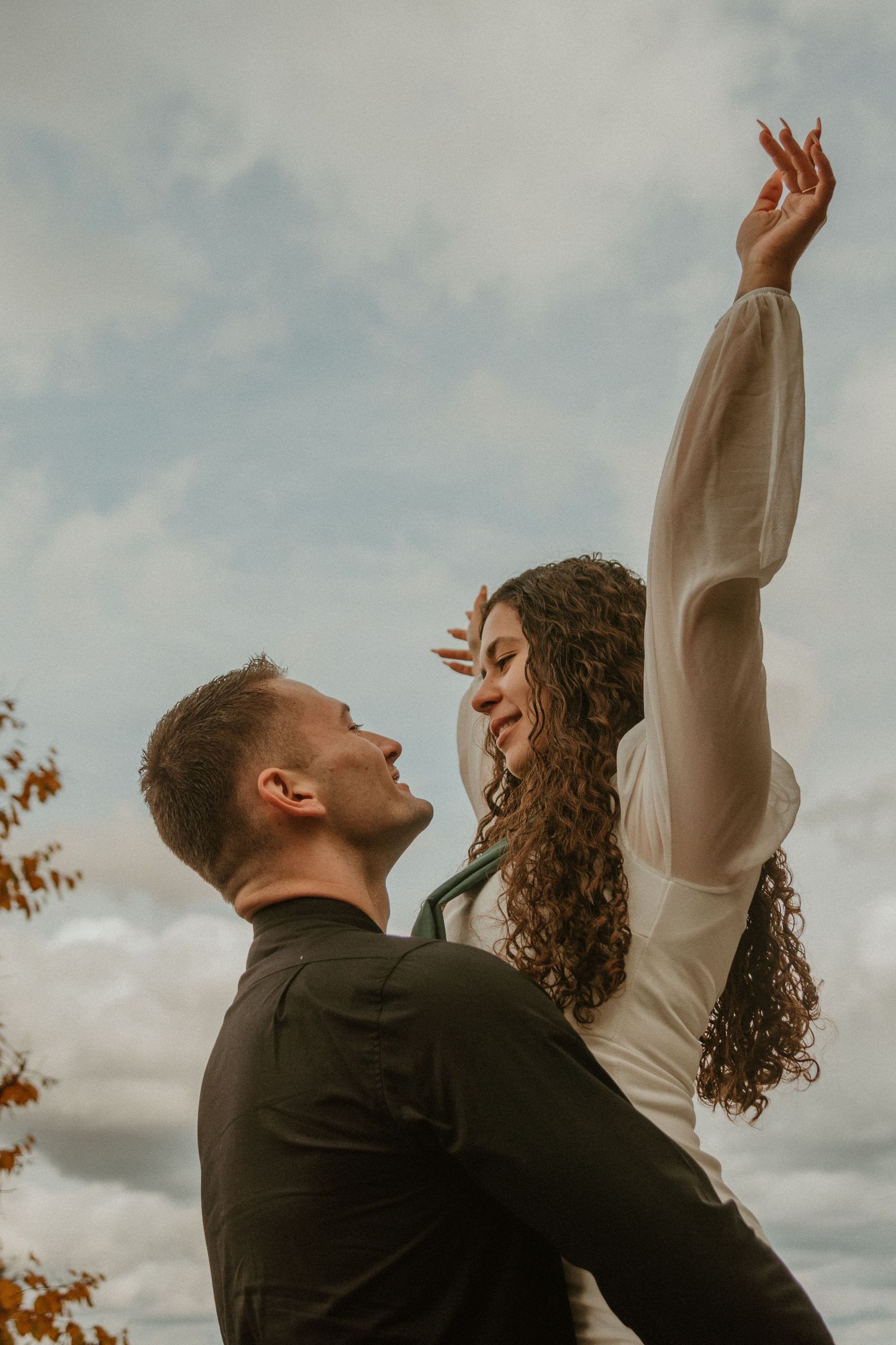 Romantic couple dancing and twirling together against a cloudy sky.