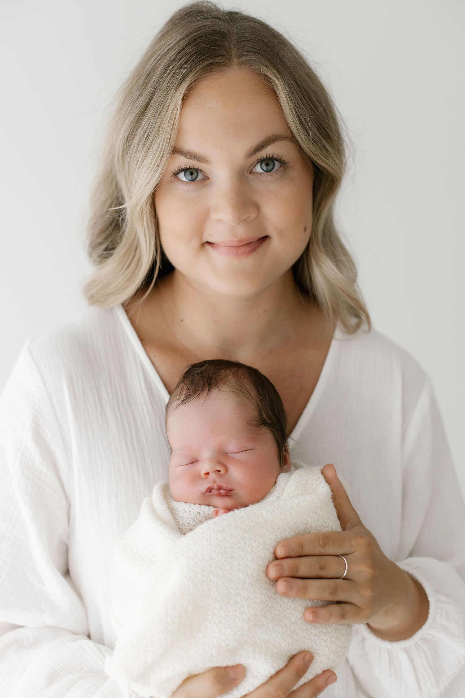 Suloinen vauva kauniin äitinsä sylissä kasvot kuvaan päin newbornkuvauksessa Lahdessa
