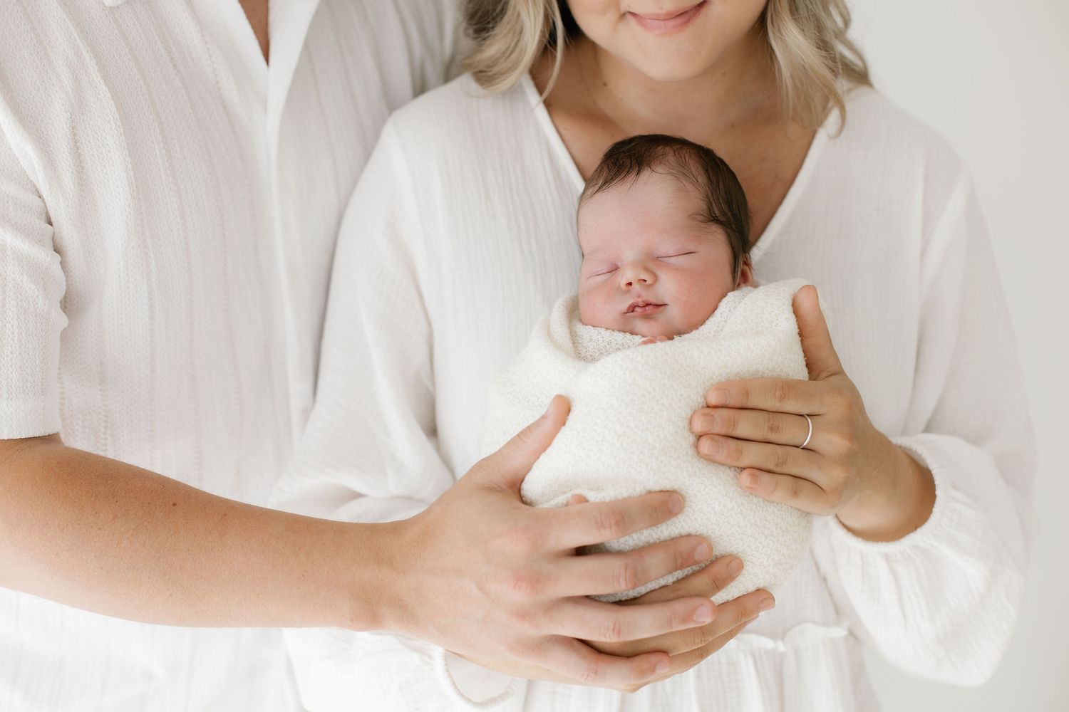 Suloinen vastasyntynyt vauva äidinsä sylissä kauniisti kapaloituna newbornkuvauksessa