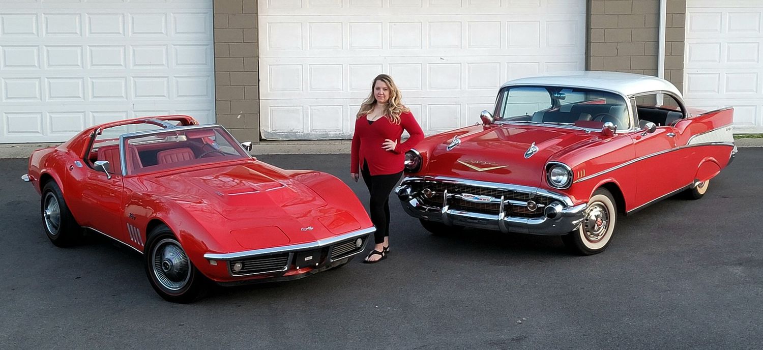 Woman standing between a two classic vintage cars, A 1968 Chevrolet Corvette and a 1957 Chevrolet Bel Air in front of a garage