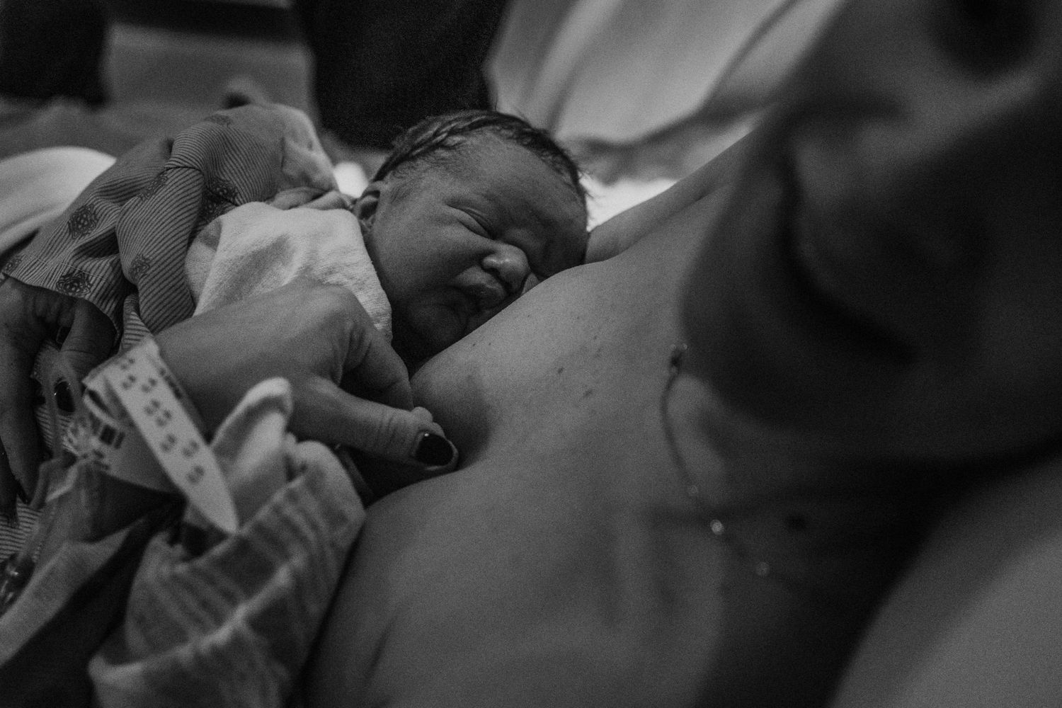 A newborn baby sleeps peacefully in black and white while resting skin-to-skin with their caregiver.